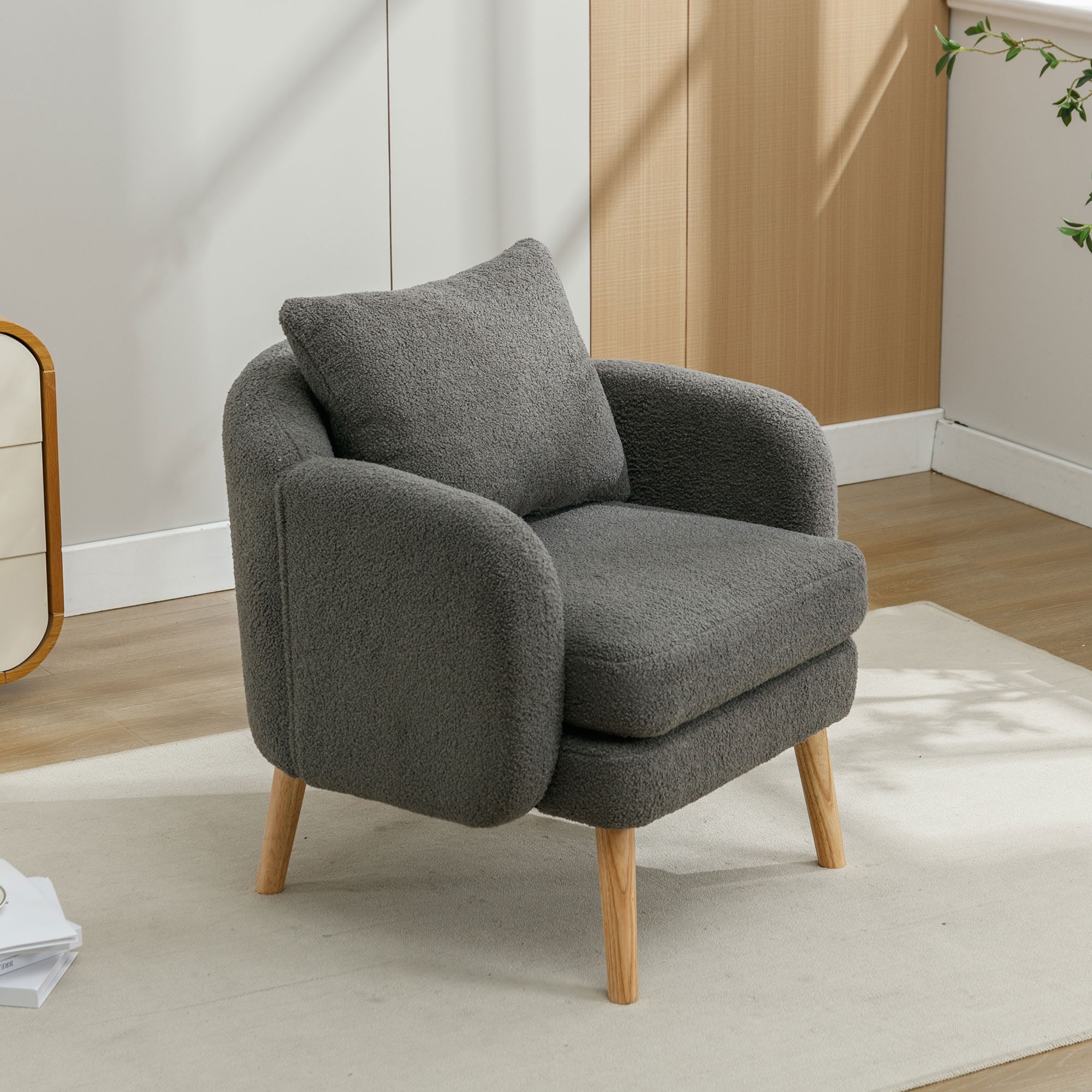 Gemütlicher grauer Sessel mit Holzbeinen und passendem Kissen, auf einem hellen Teppich platziert.