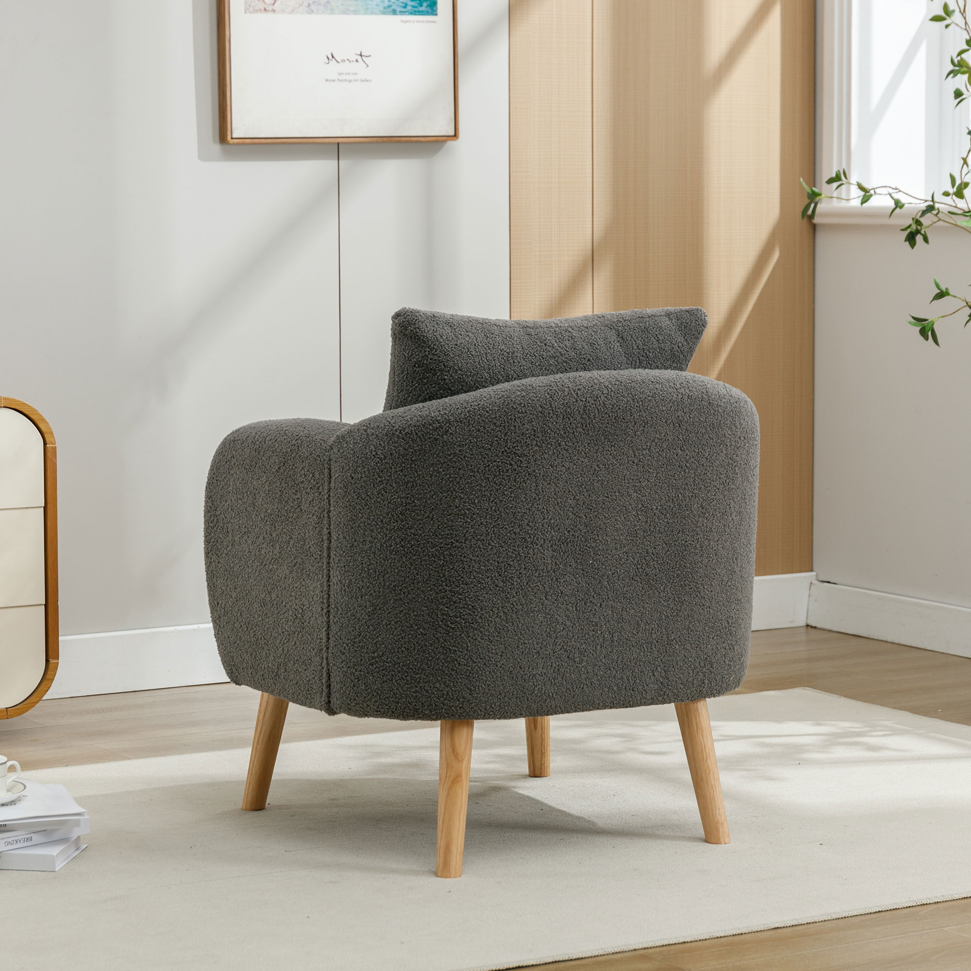 Ein gemütlicher grauer Sessel mit Holzbeinen, auf einem hellen Teppich. Im Hintergrund ein Gemälde.