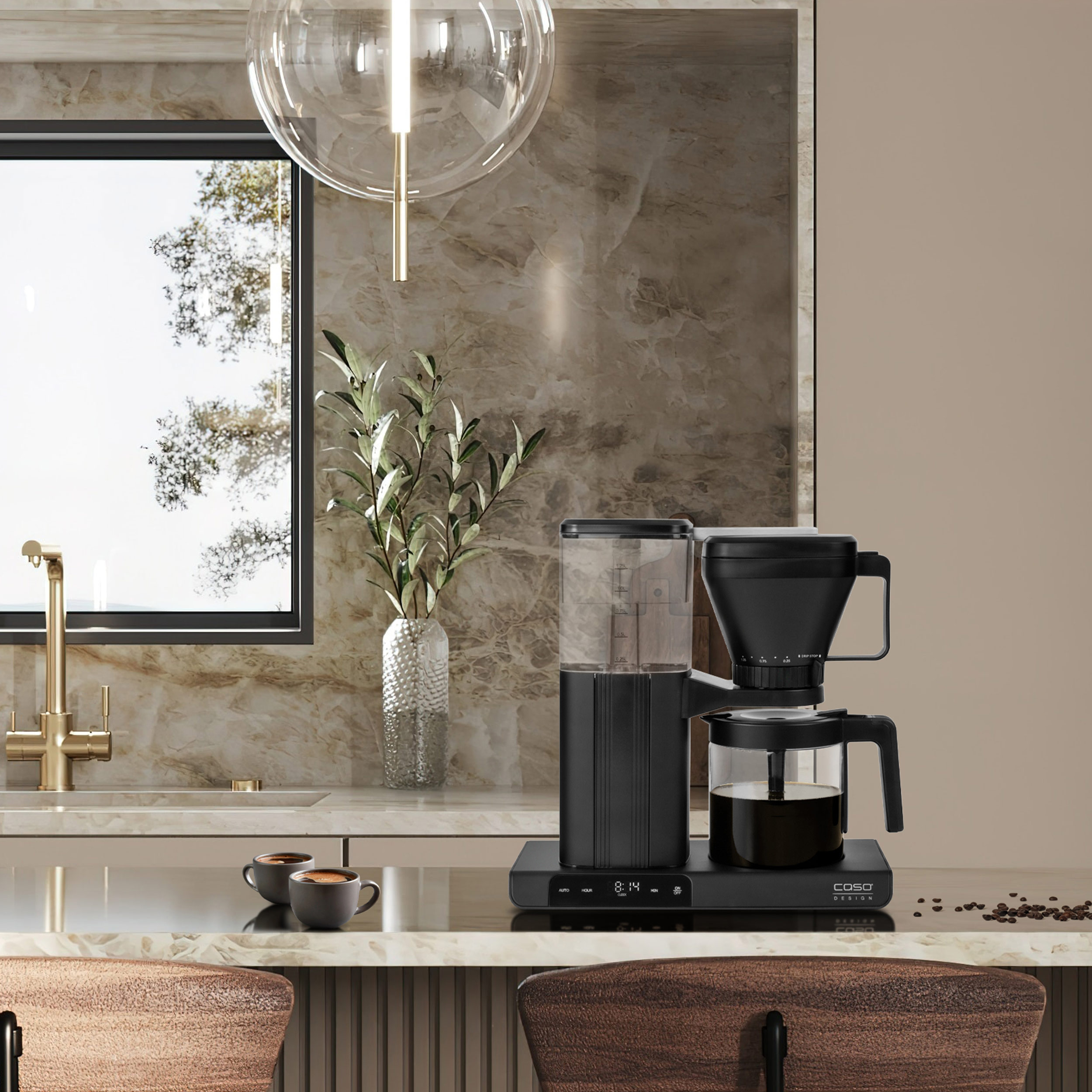 Eine schwarze Kaffeemaschine auf einer Küchentheke, mit einer Kaffeekanne und zwei Tassen im Vordergrund.