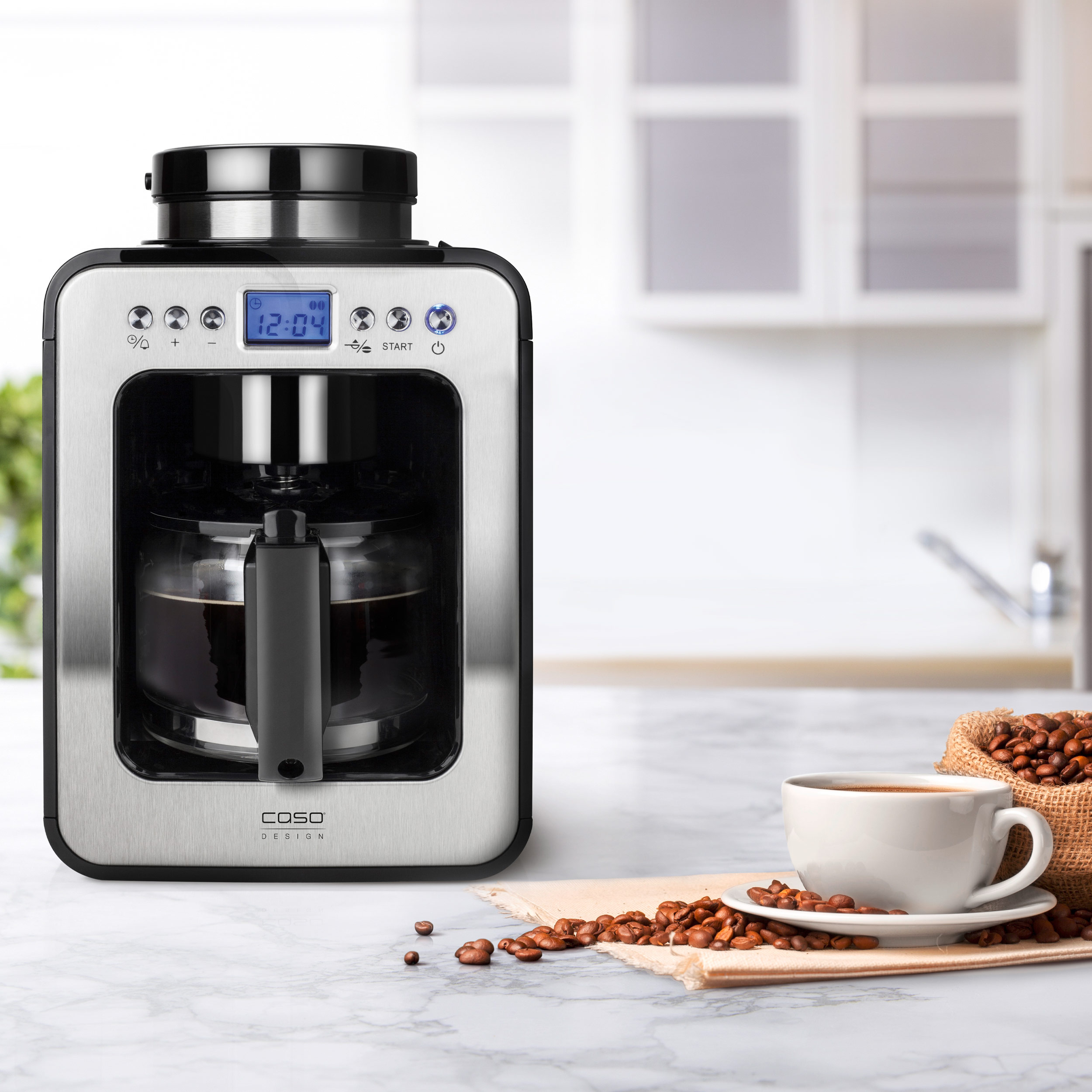 Cafetera sobre encimera de mármol con taza de café, granos y fondo de cocina claro.