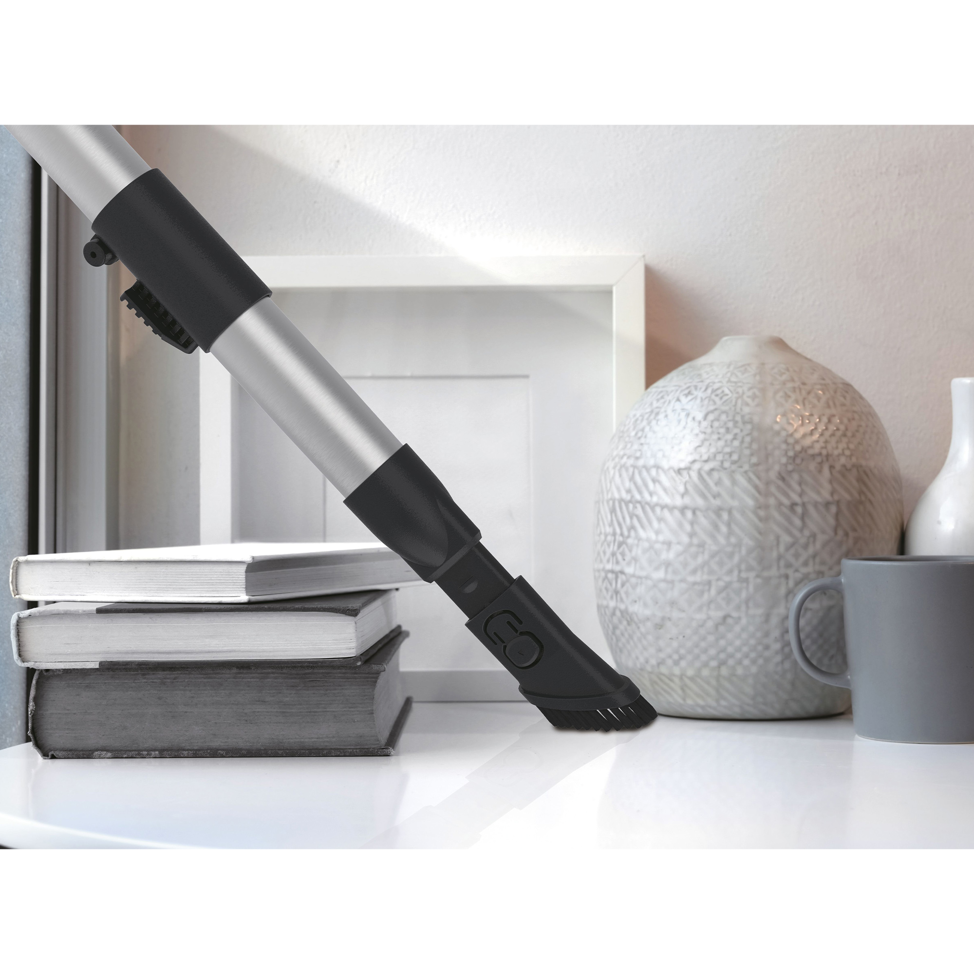 Końcówka odkurzacza na białej powierzchni z książkami i kubkiem w tle.