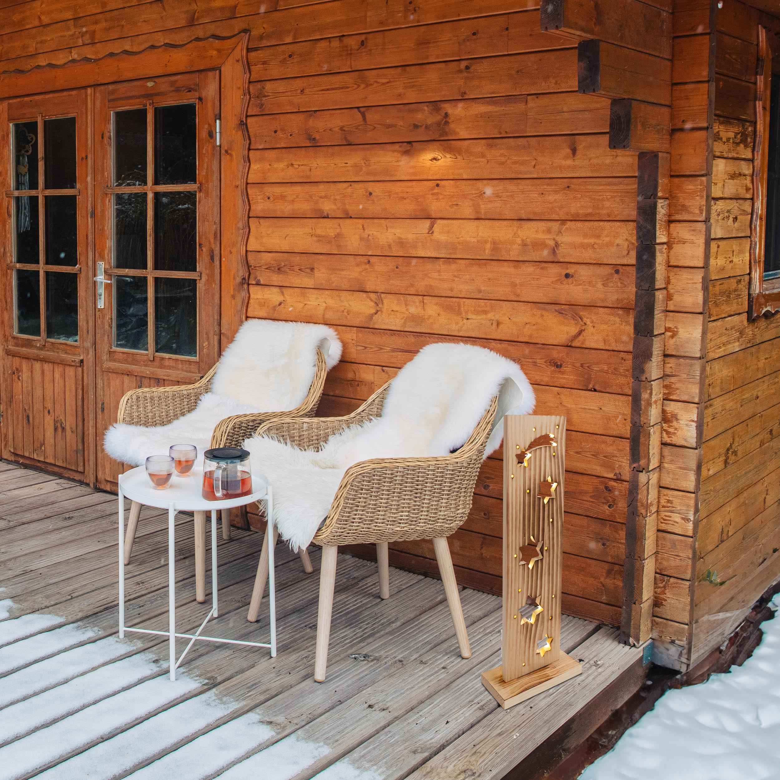 Holzhütten-Außenbereich mit Stühlen, Tisch und Holzstern-Dekoration. Schnee liegt auf dem Boden.