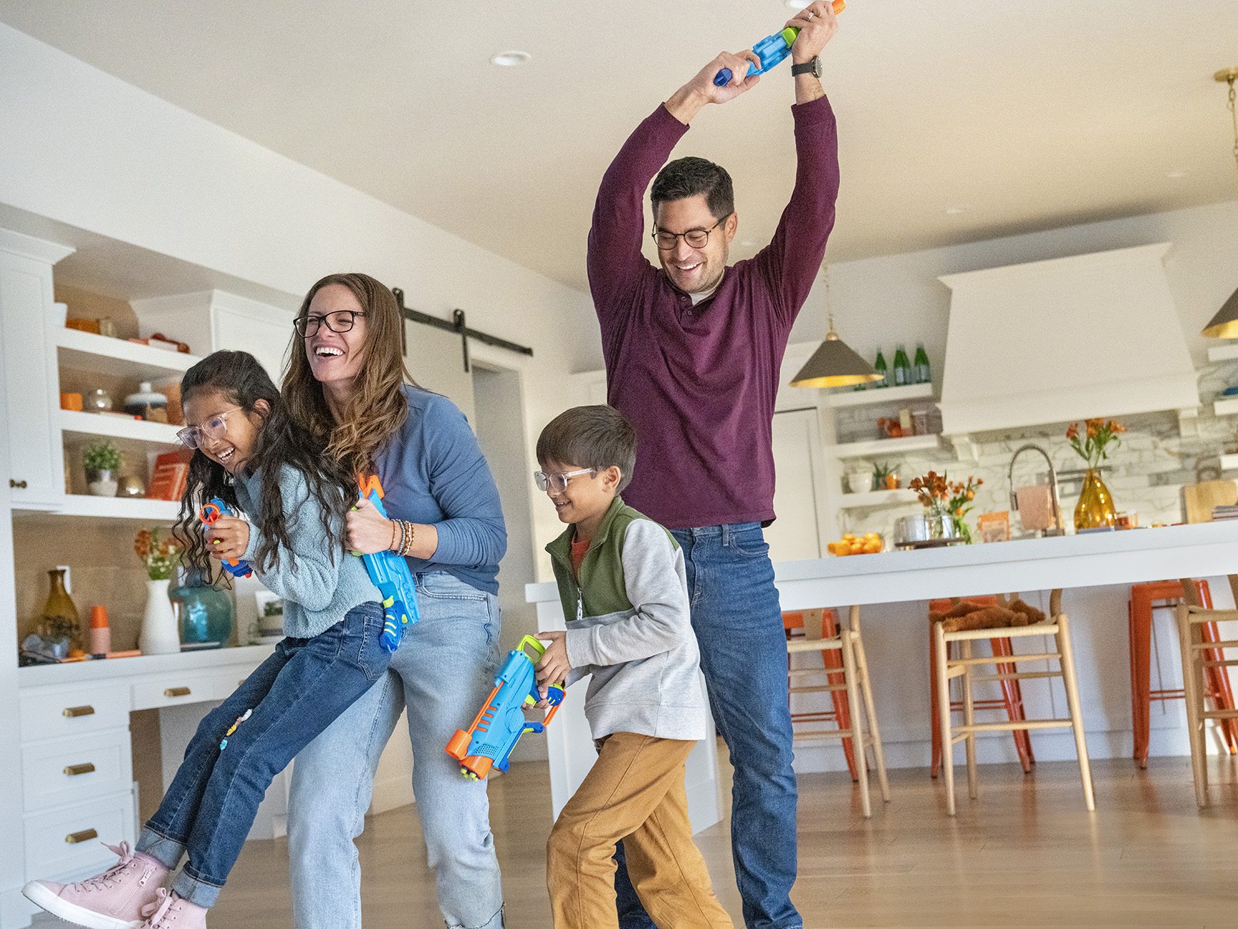 Una famiglia gioca con pistole ad acqua giocattolo in una stanza luminosa, sorridendo e ridendo.
