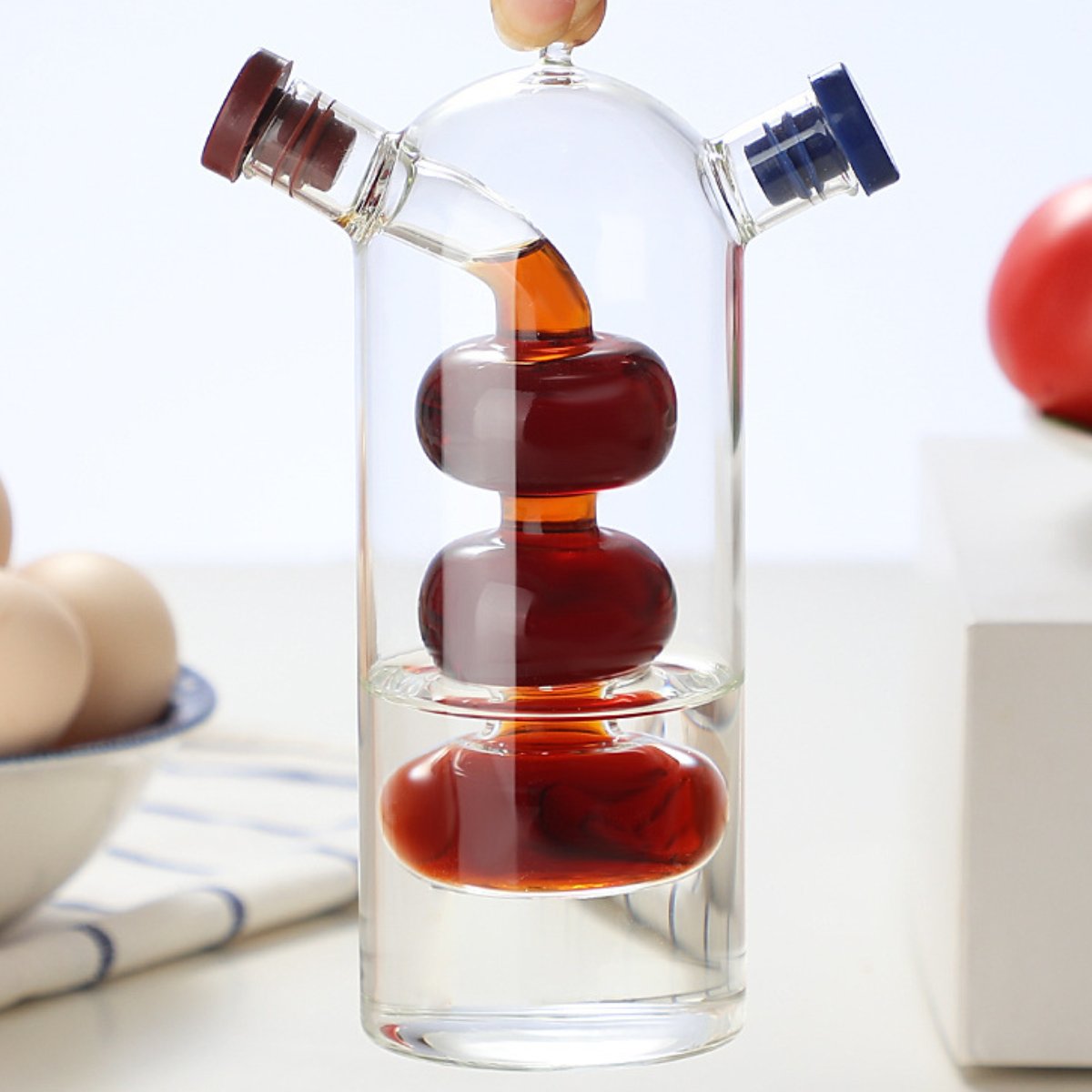 Transparente Glasölflasche mit zwei Ausgüssen, gefüllt mit rötlicher Flüssigkeit.