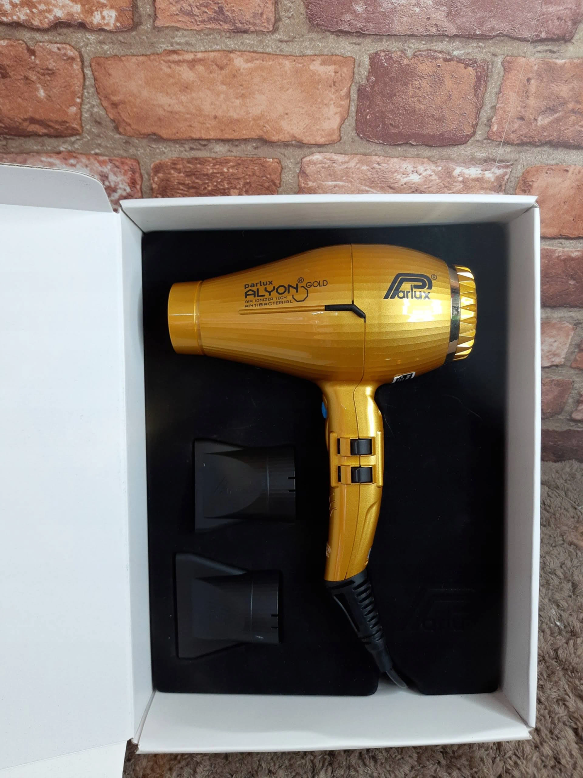 Goldener Haartrockner in einer weißen Box. Zwei schwarze Düsen sind sichtbar.