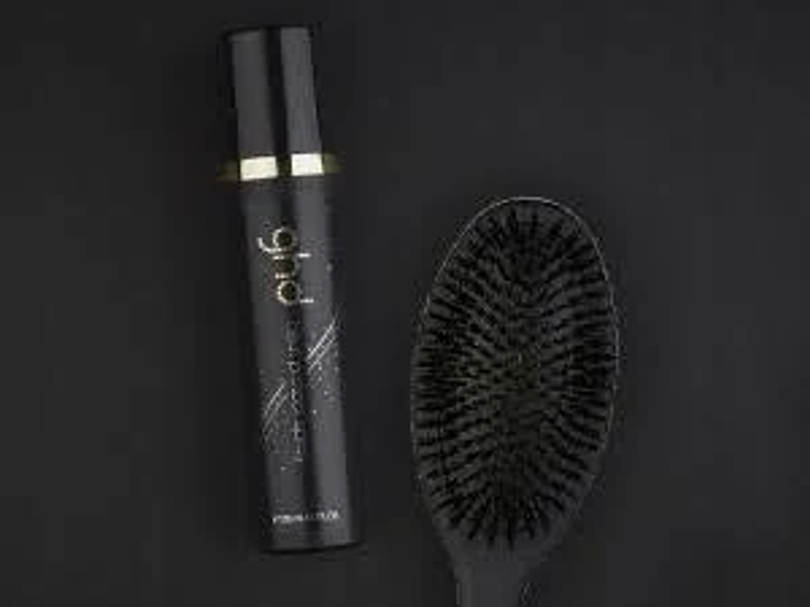 Czarny produkt do włosów ghd i czarna szczotka ghd. Oba na ciemnym tle.