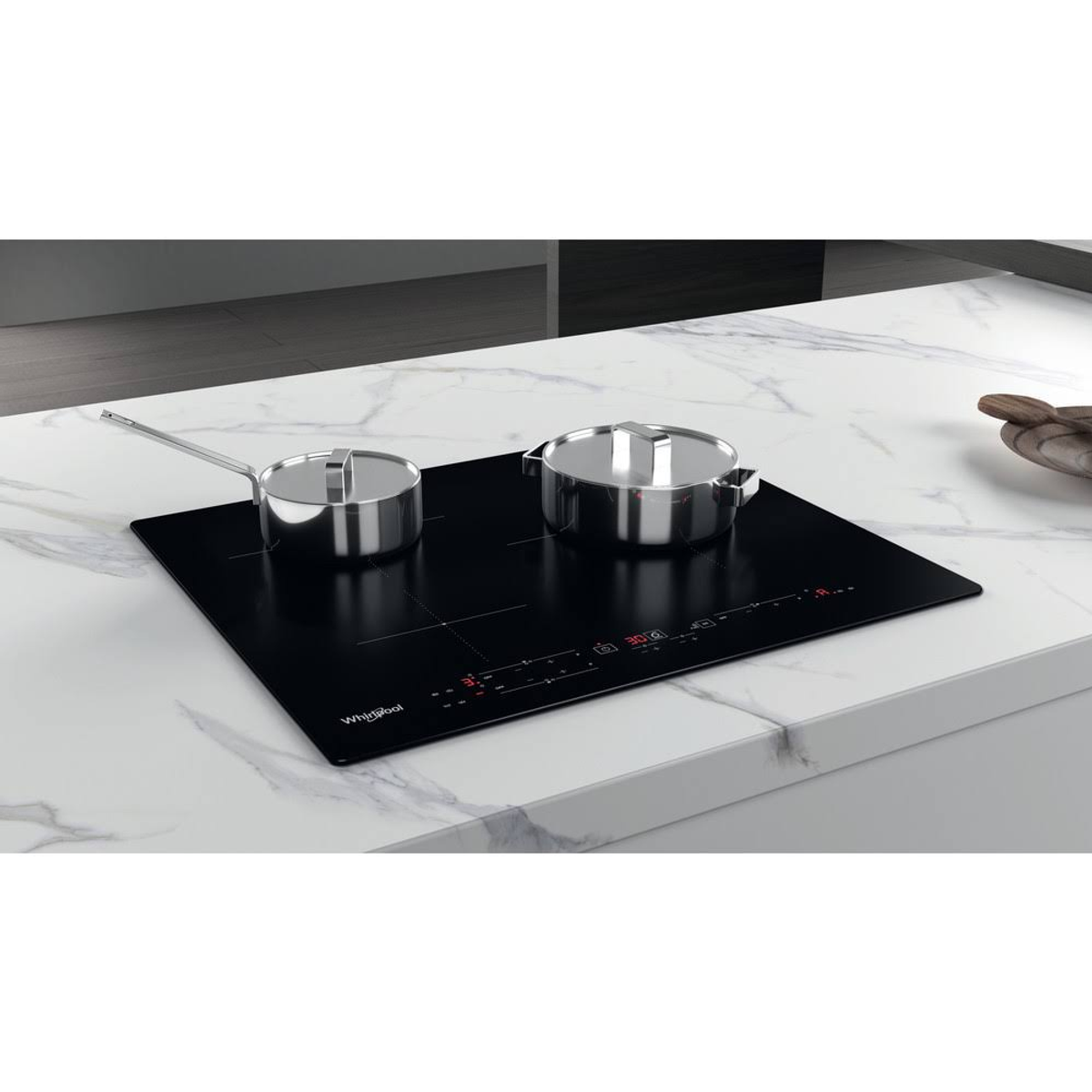 Placa de cocina negra con dos ollas plateadas. Está sobre una encimera de mármol. El logotipo de Whirlpool es visible.