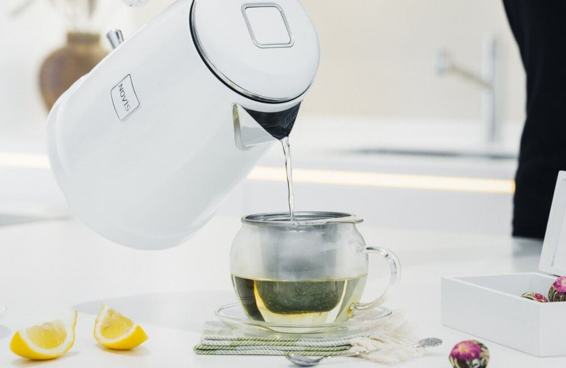 Weißer Wasserkocher gießt Wasser in eine Teetasse.