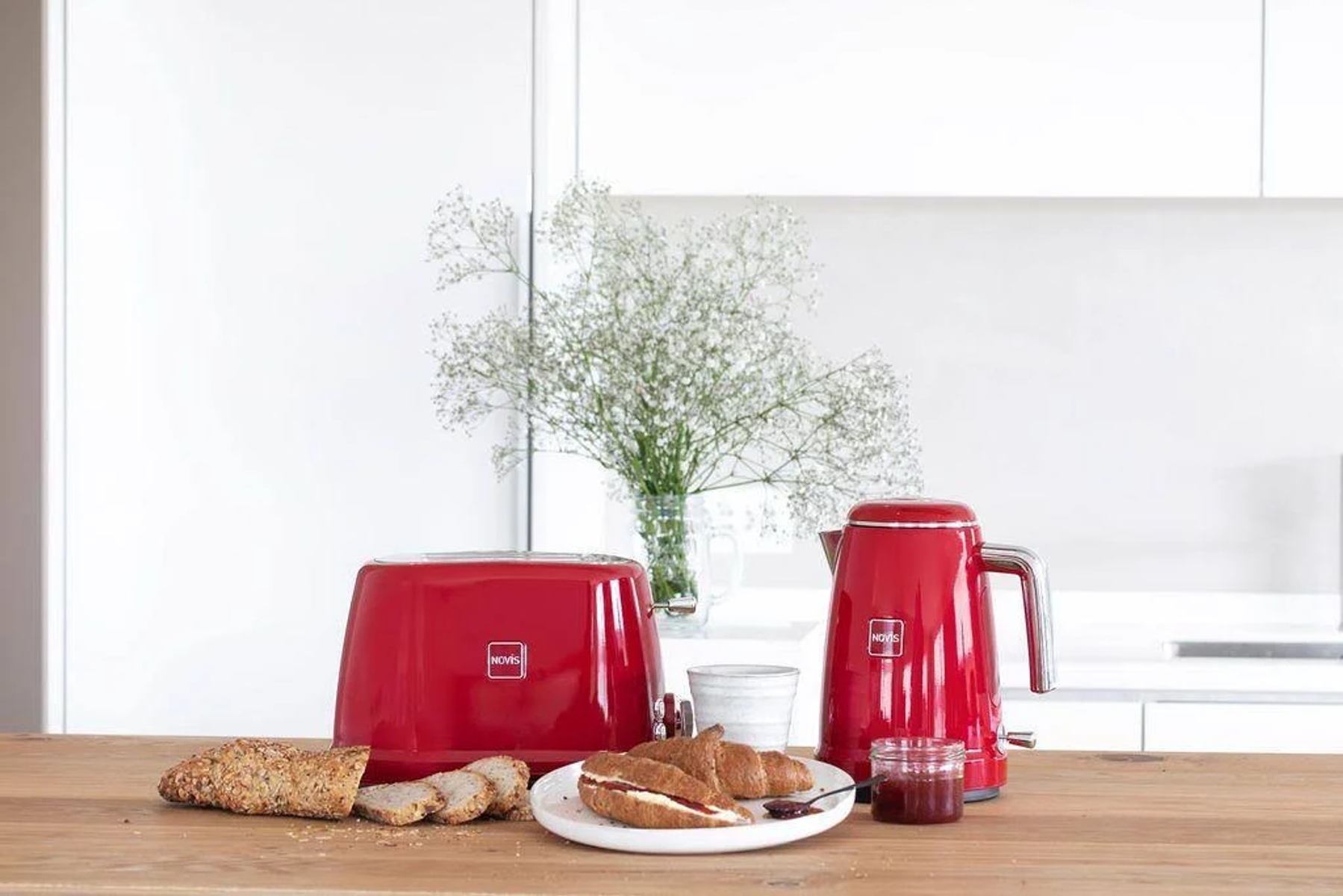 Set da cucina rosso: bollitore, tostapane, pane e croissant su un tavolo di legno.