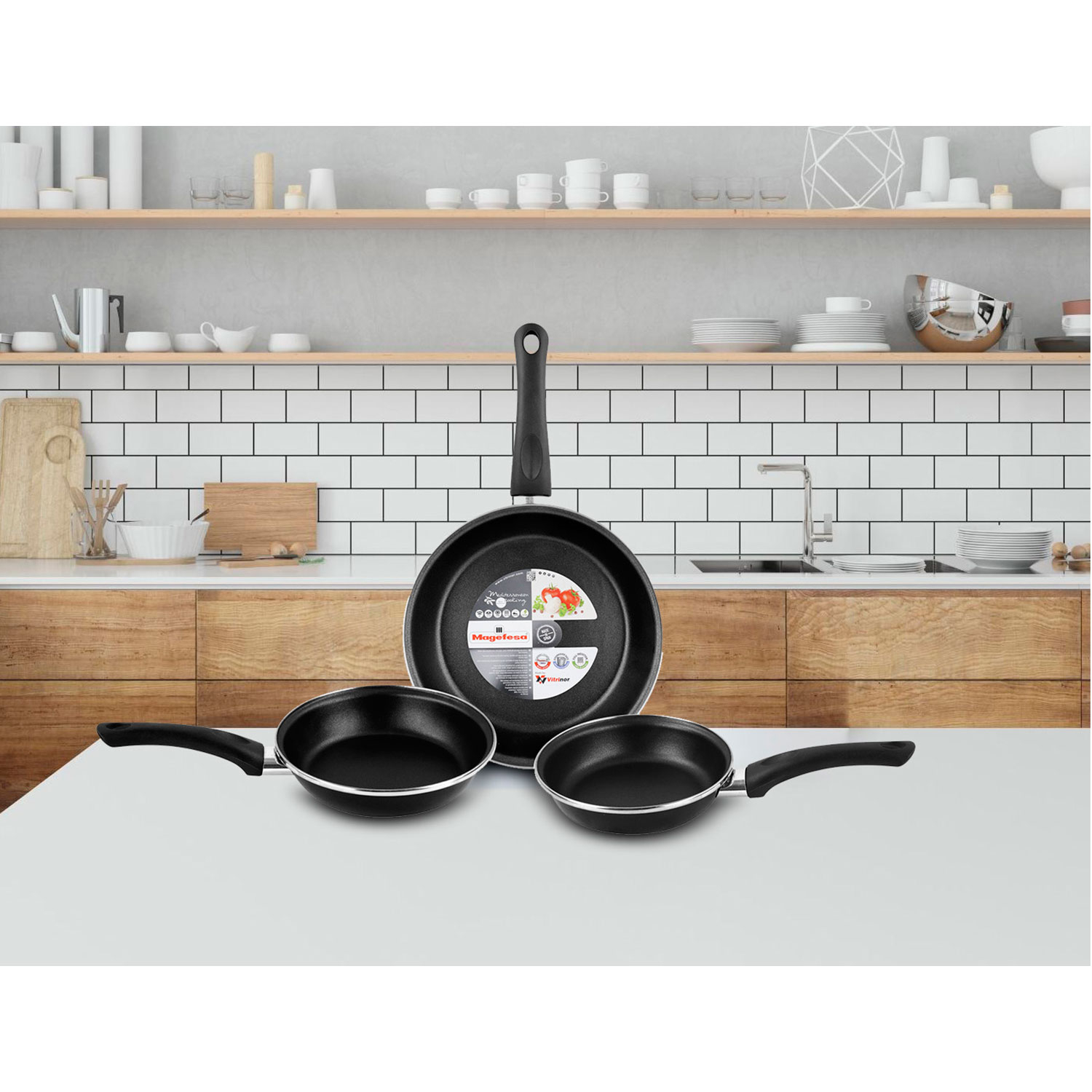 Un juego de tres sartenes negras de diferentes tamaños sobre una superficie blanca en una cocina.