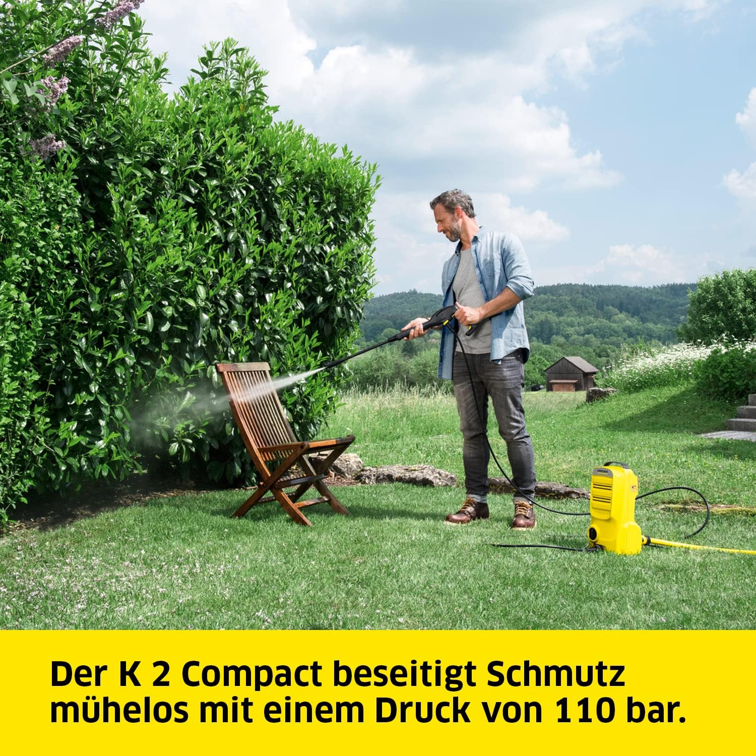 Ein Mann reinigt einen Holzstuhl mit einem Hochdruckreiniger in einem grünen Garten.