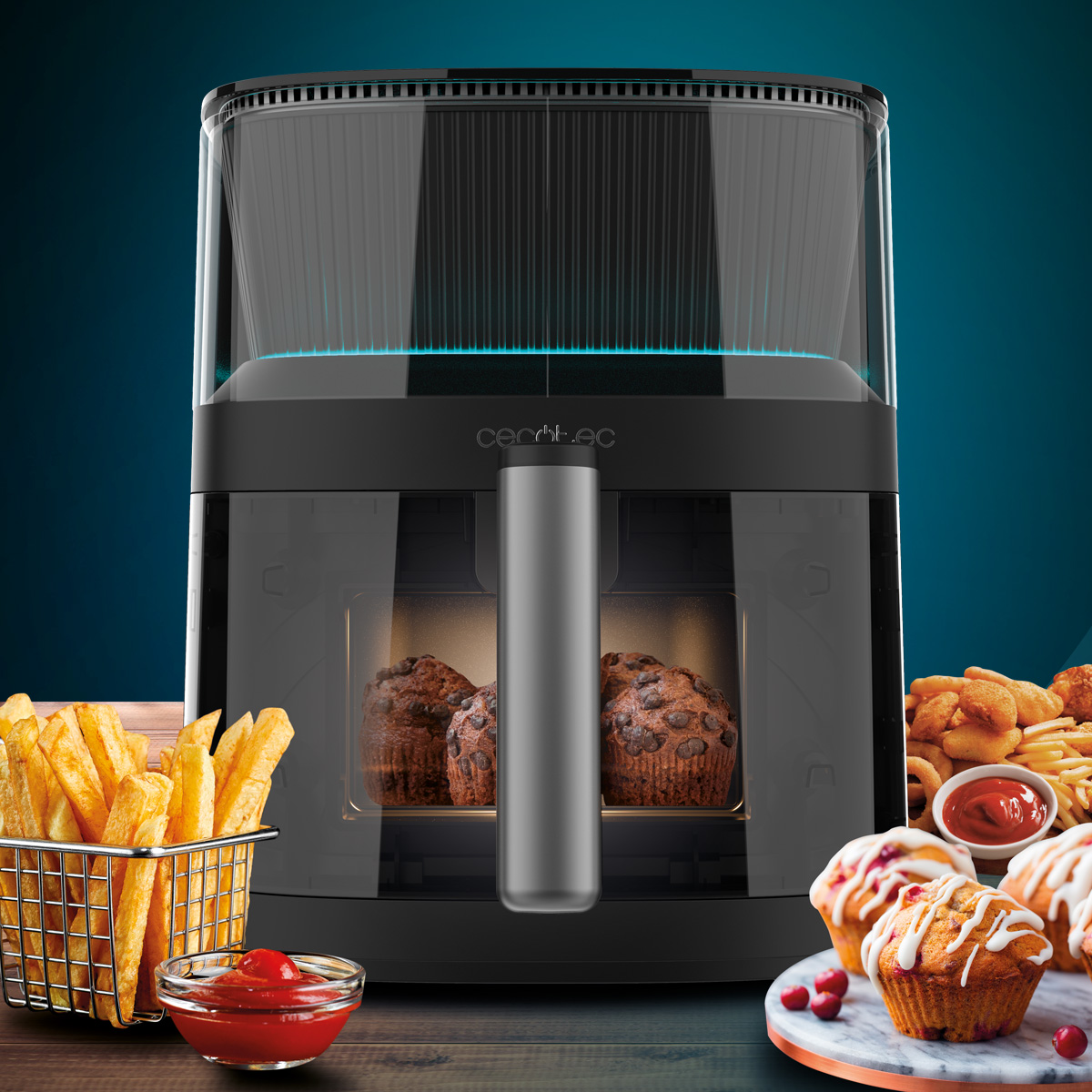 Zwarte airfryer met transparante voorkant. Muffins en friet staan op de voorgrond met ketchup.