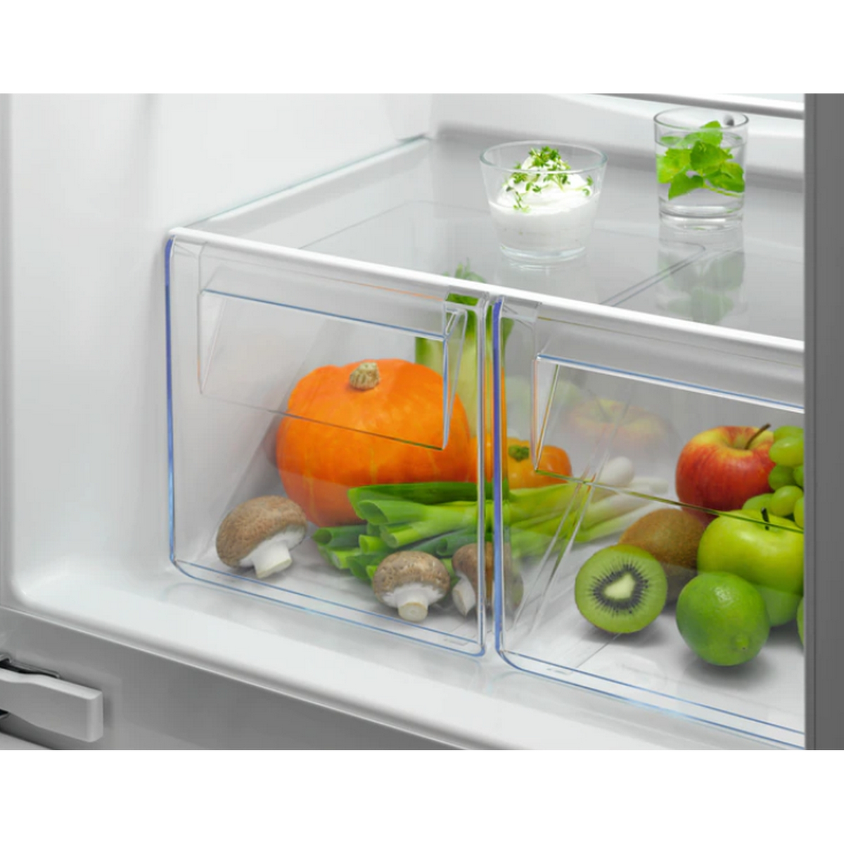 Interior de frigorífico con recipientes transparentes que contienen verduras, una calabaza y un vaso con hierbas.