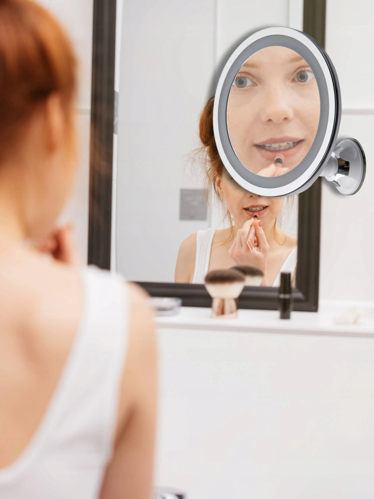 Frau, die in einen beleuchteten Spiegel schaut und Lippenstift aufträgt. Ein zweiter Spiegel spiegelt ihr Gesicht wider.
