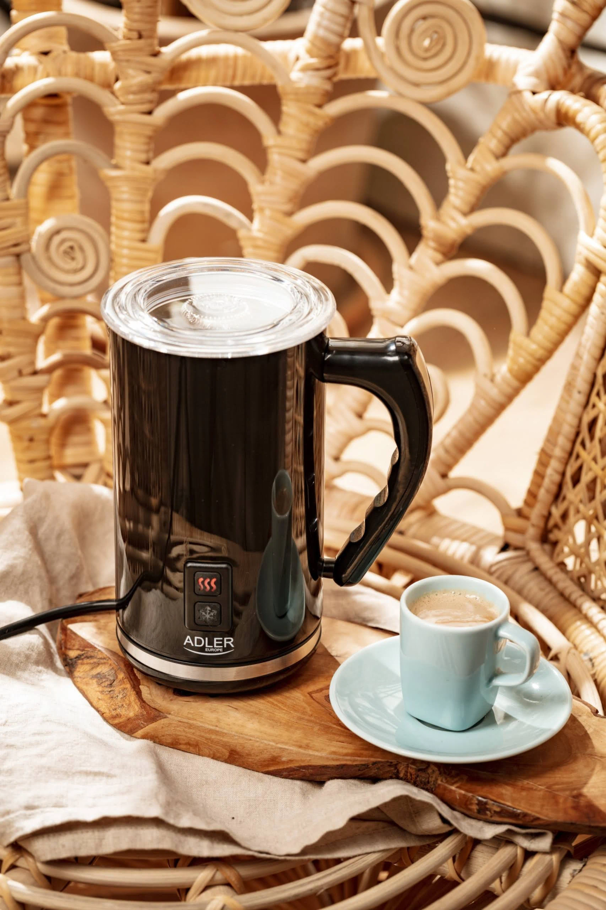 Czarny spieniacz do mleka z filiżanką kawy, na drewnianej desce i plecionym krześle.