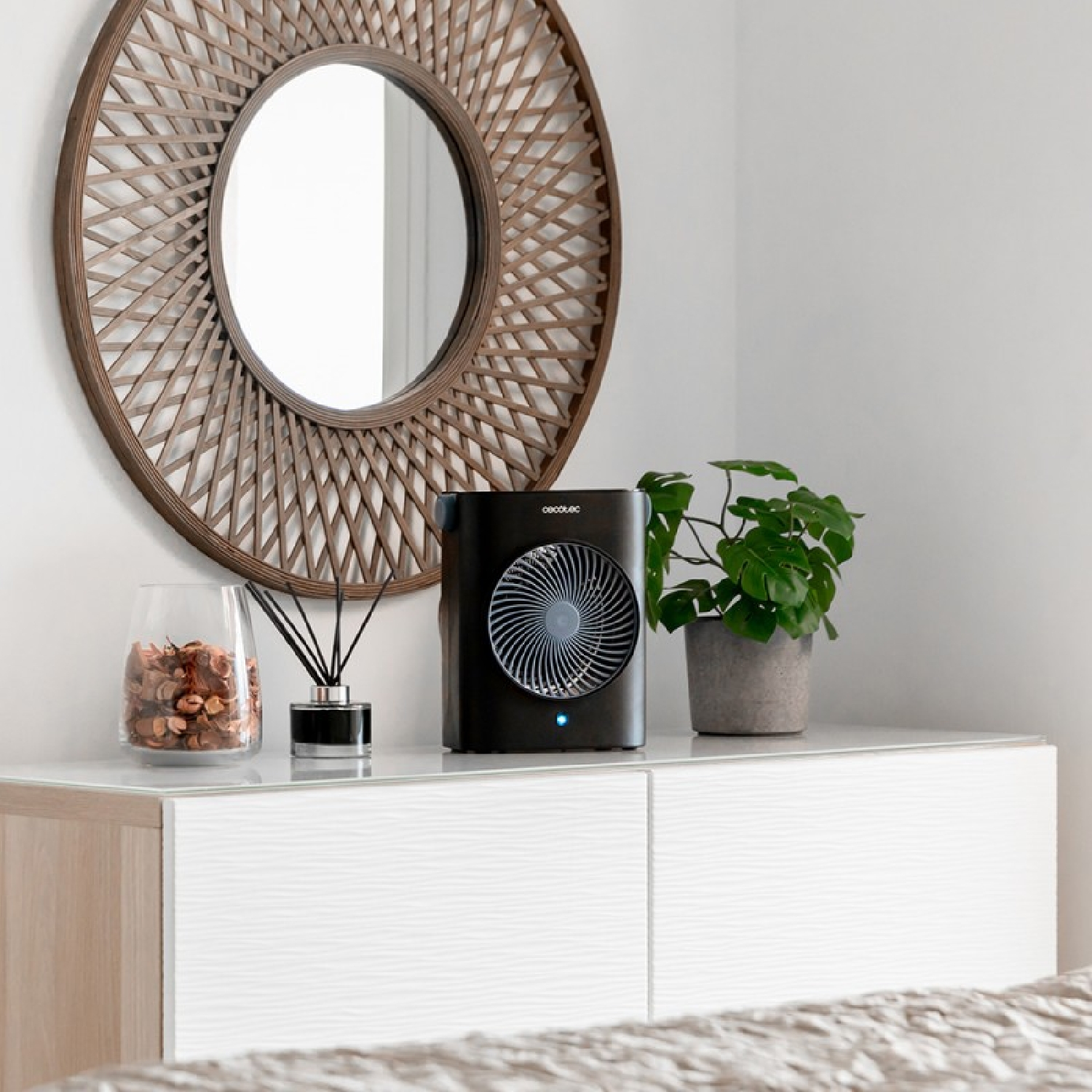 Czarny wentylator na białej komodzie, z lustrem i rośliną w tle.