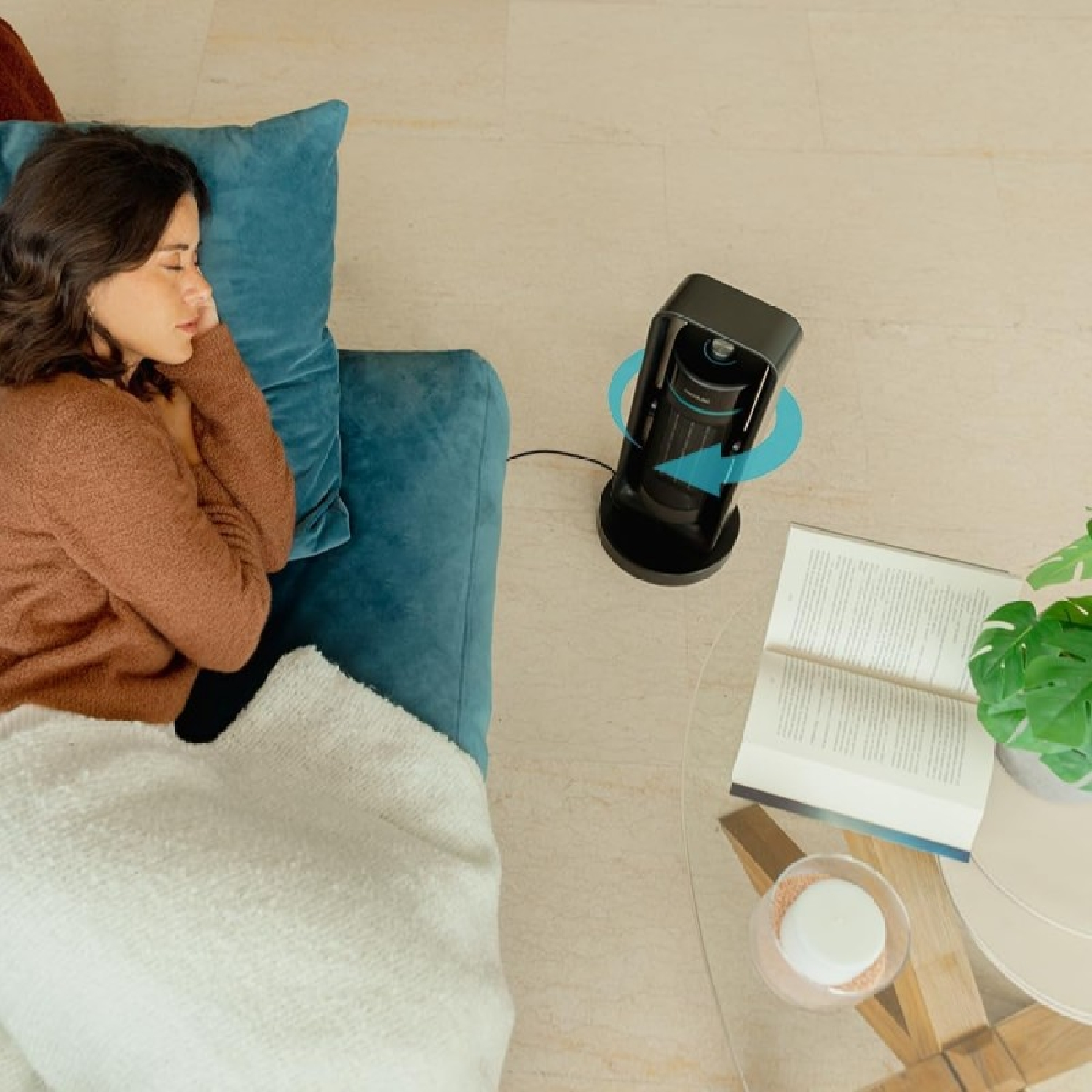 Frau schläft auf blauem Sofa mit Ventilator in der Nähe und einem Buch. Draufsicht.