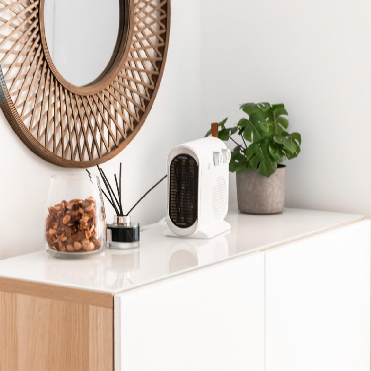 Mobile bianco, specchio e piccolo termoventilatore. Pianta e decorazioni sul mobile.
