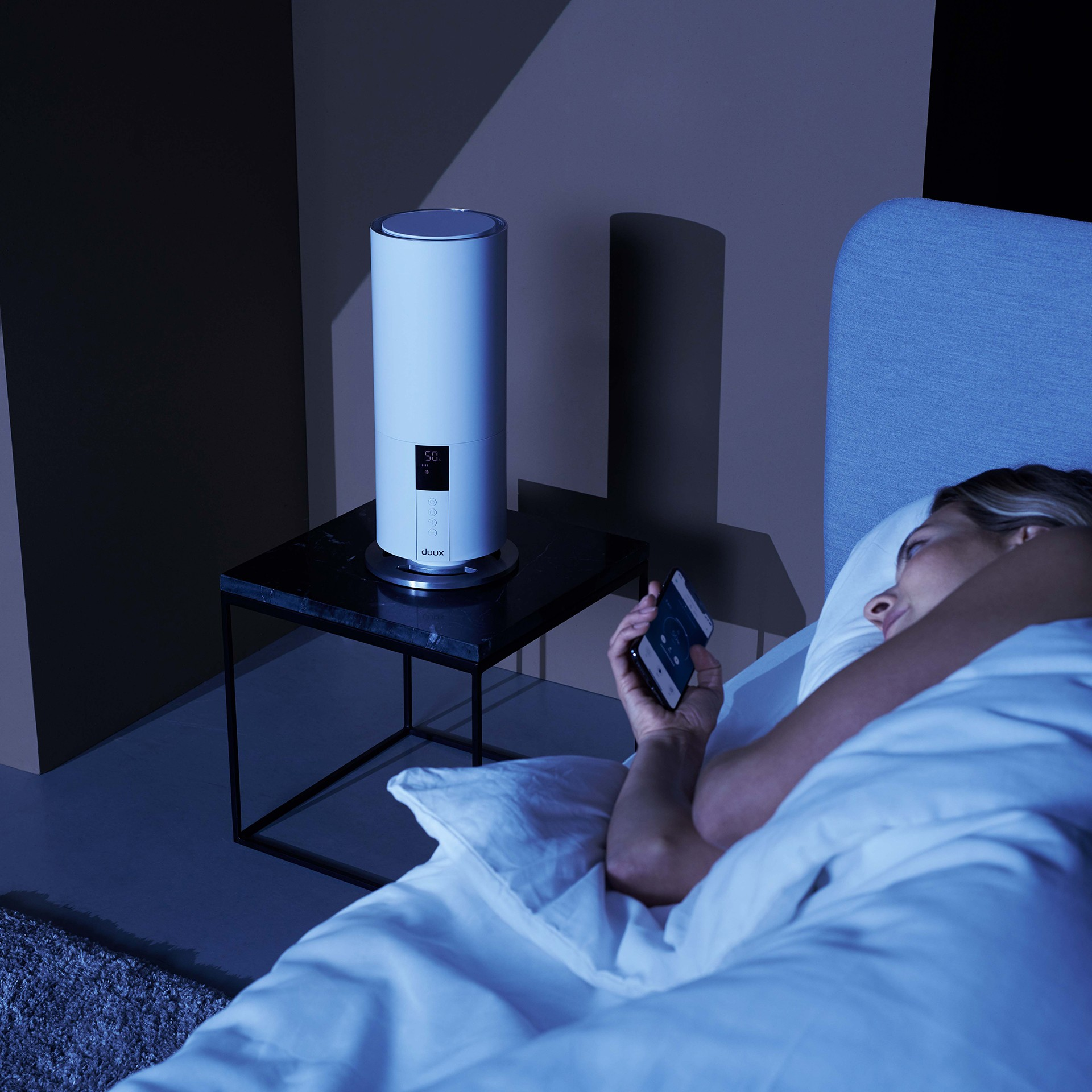 Kobieta w łóżku patrząca na telefon obok nawilżacza.