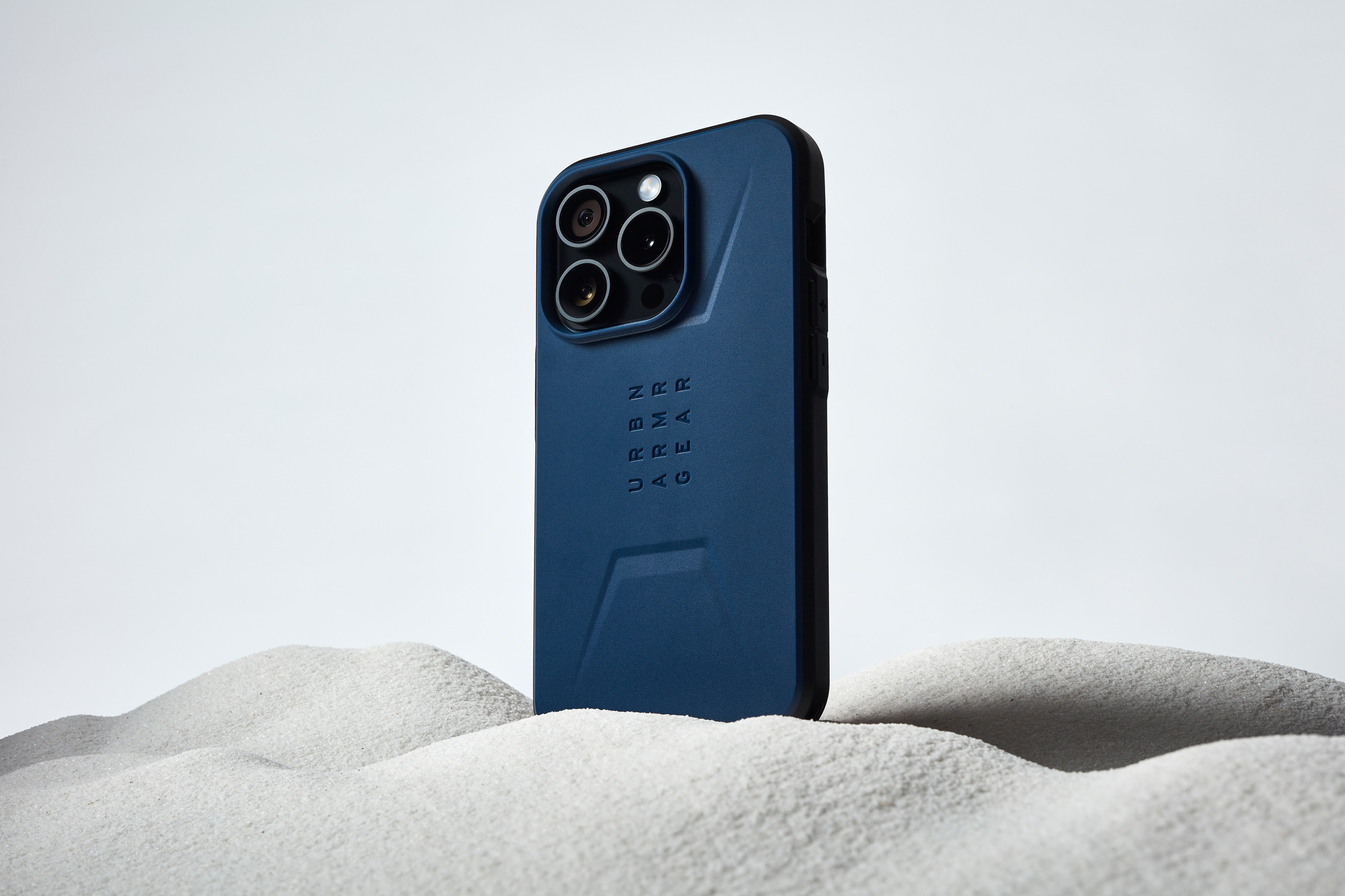 Blaue Handyhülle auf Sand. Telefon hat drei Kameras.