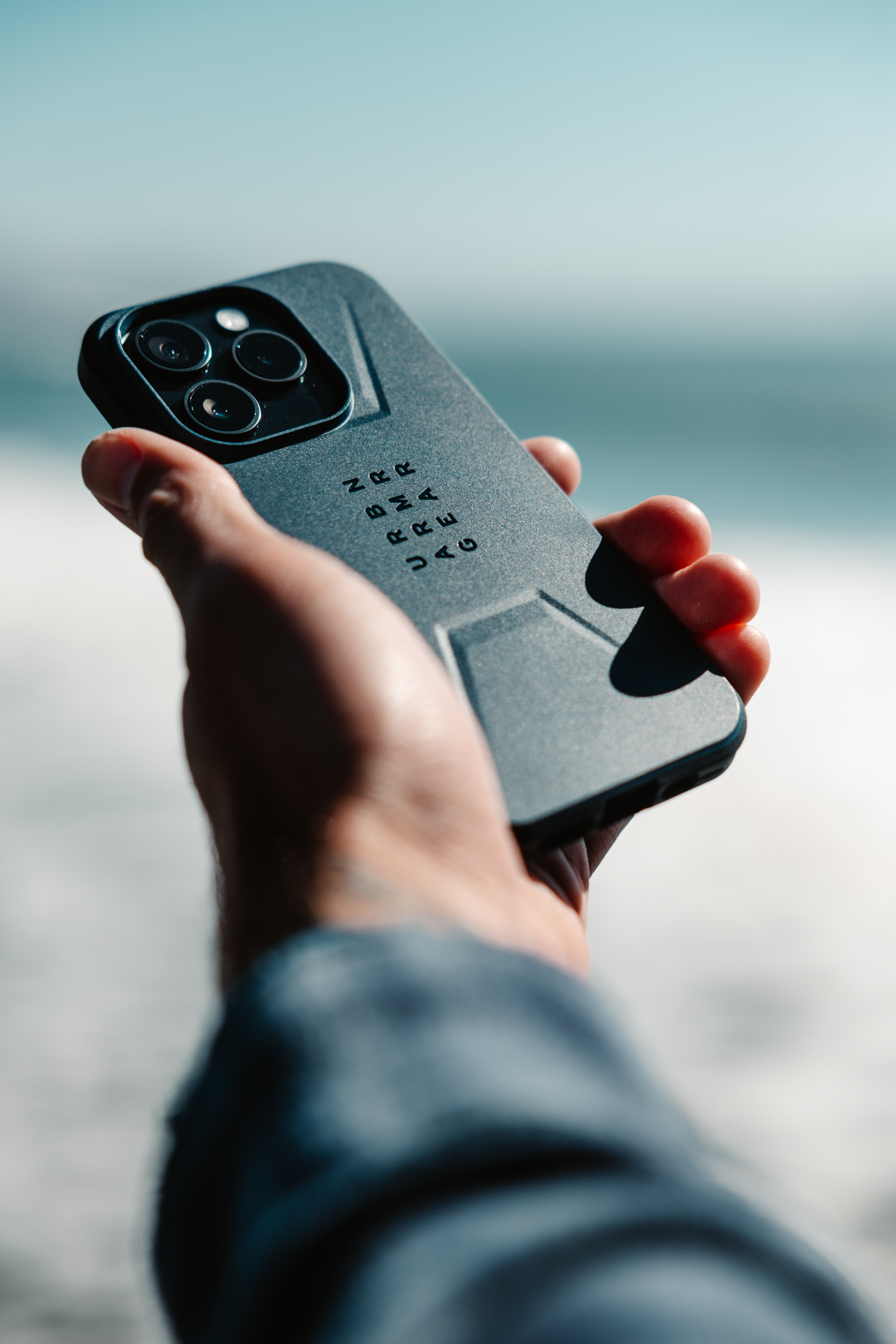 Hand, die ein schwarzes Telefon mit Dreifachkameras und Hülle hält.