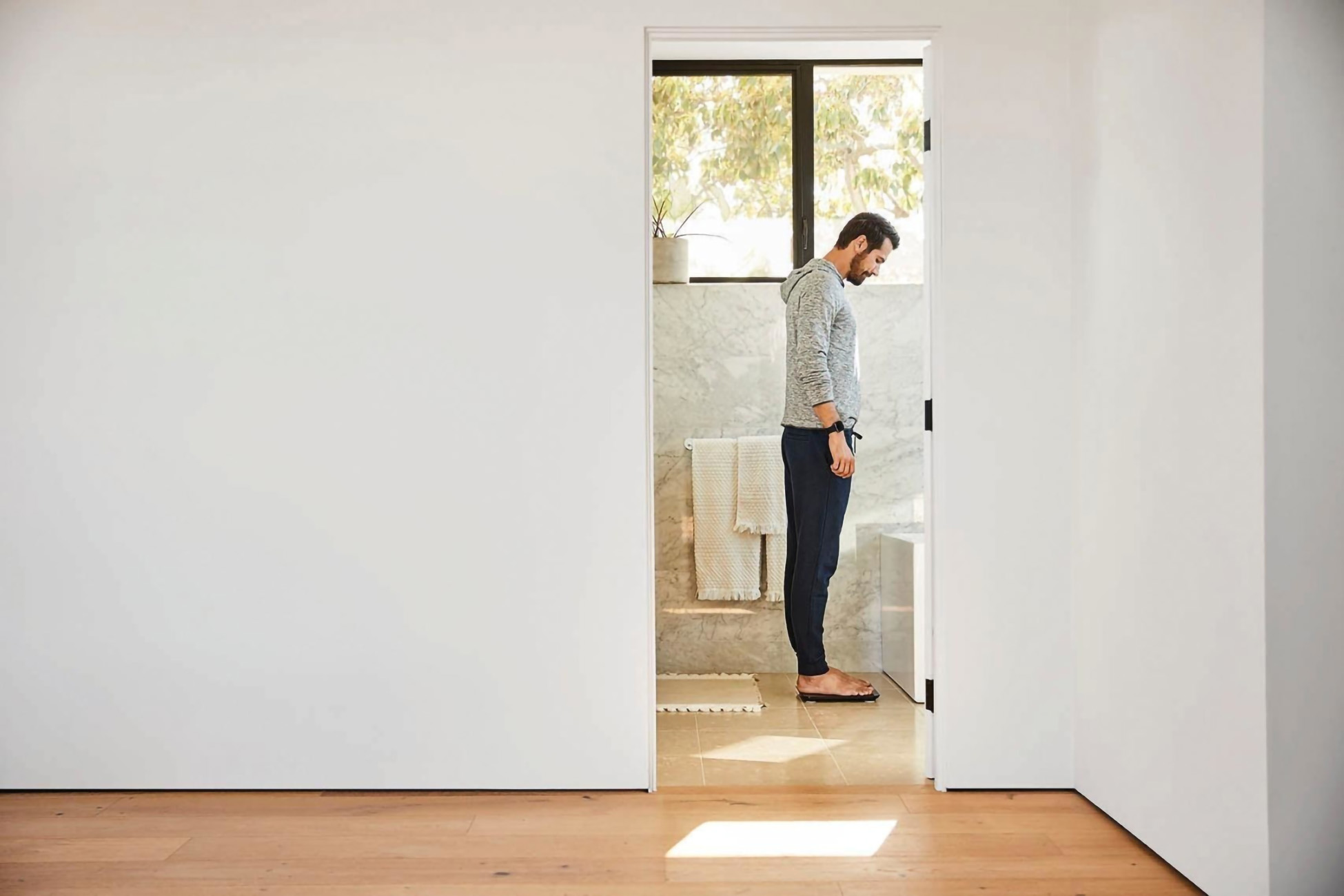 Mężczyzna stojący w drzwiach łazienki, patrzący w dół, ubrany w strój codzienny.