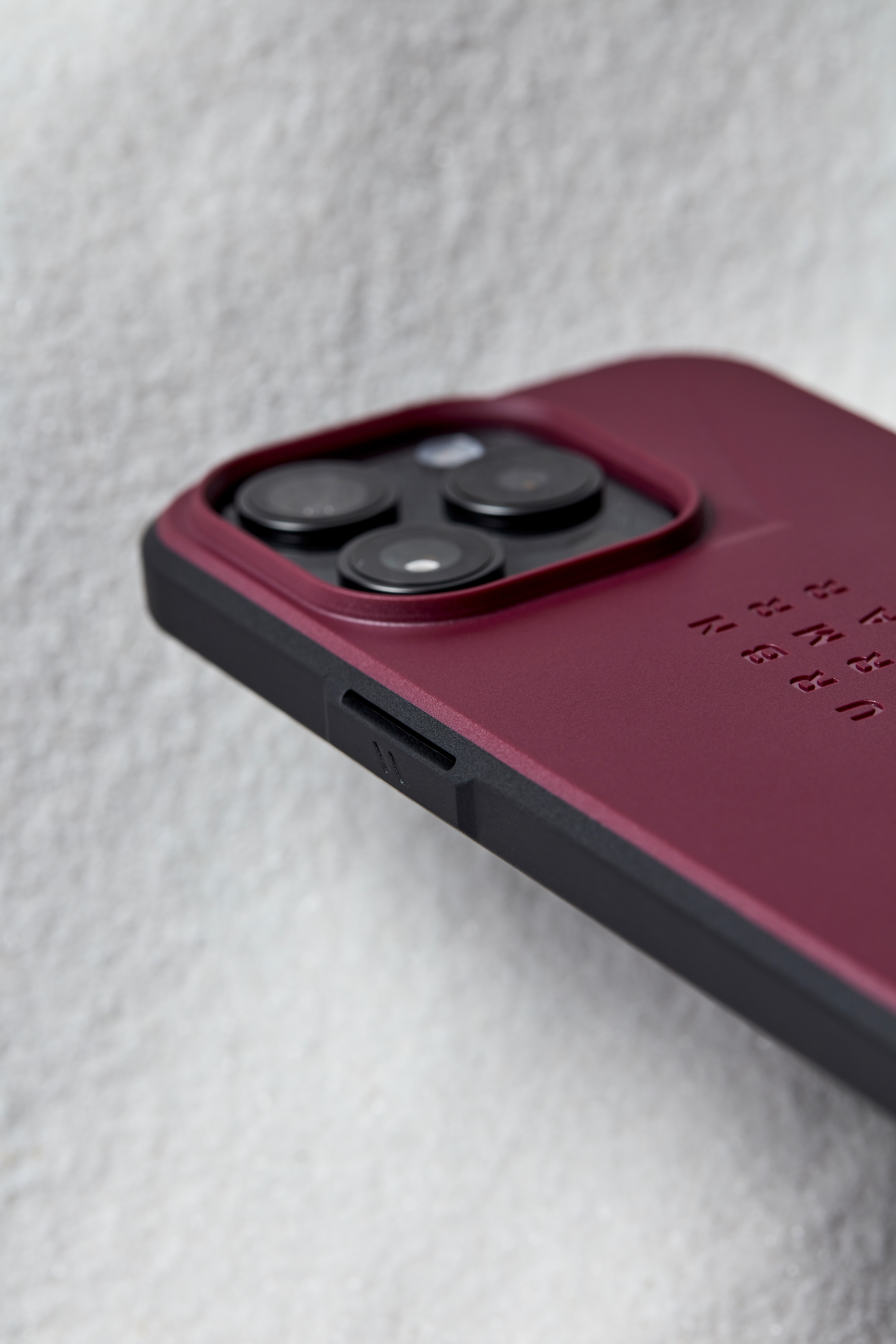 Nahaufnahme eines weinroten iPhone 14 Pro mit schwarzer Schutzhülle, das die Kameralinsen zeigt.