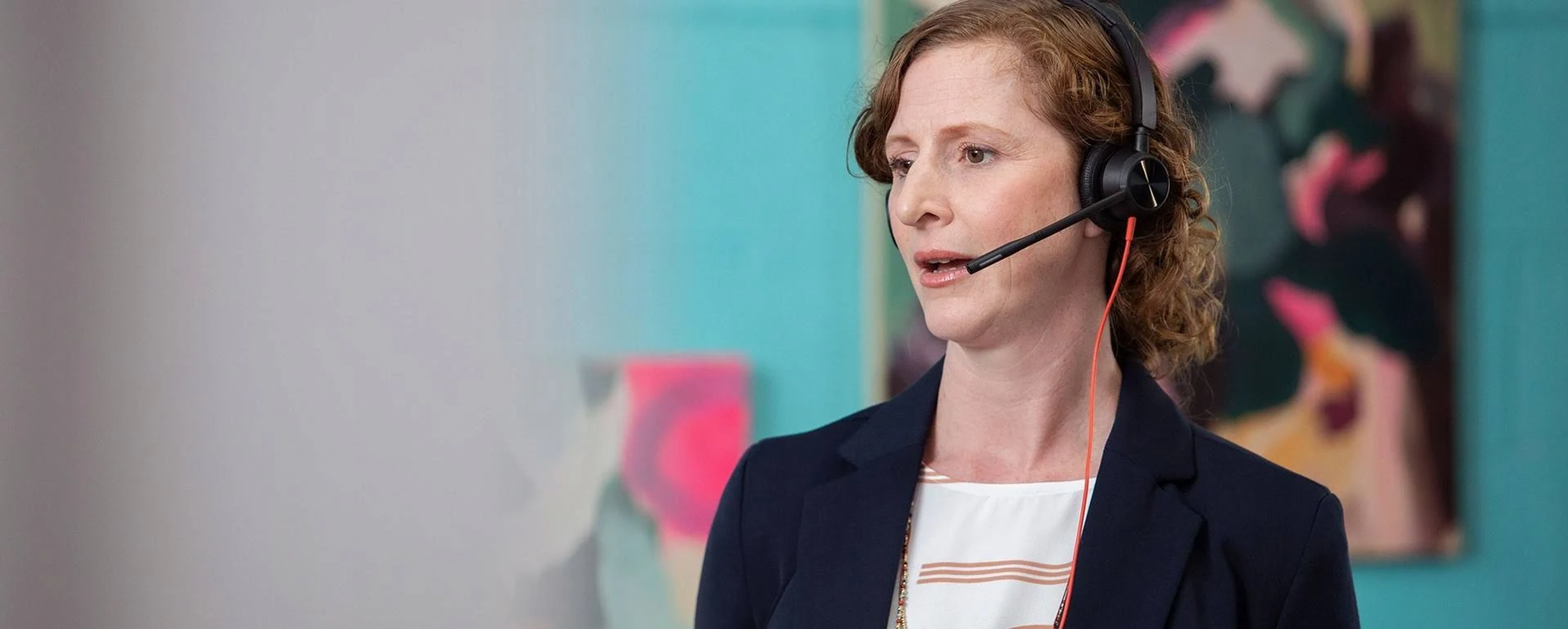 Kobieta z zestawem słuchawkowym mówi. Turkusowe tło ściany, kolorowe obrazy.