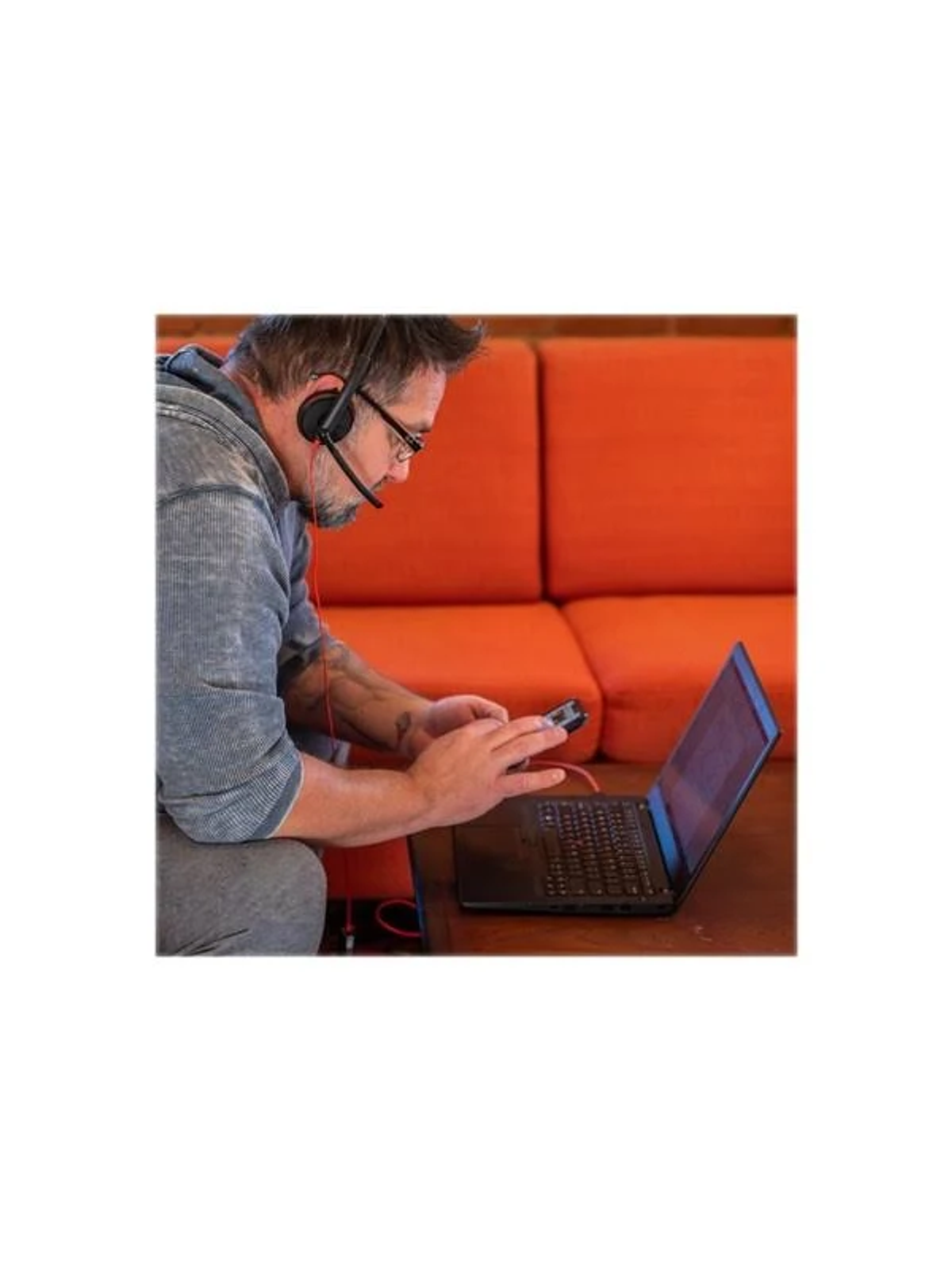 Mężczyzna w okularach i zestawie słuchawkowym korzysta z laptopa i telefonu.