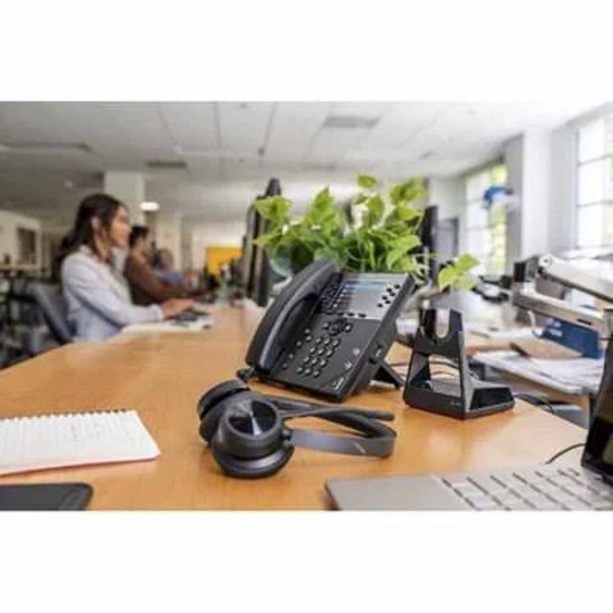 Environnement de bureau avec personnes, bureau avec casque, téléphone, bloc-notes et ordinateur.