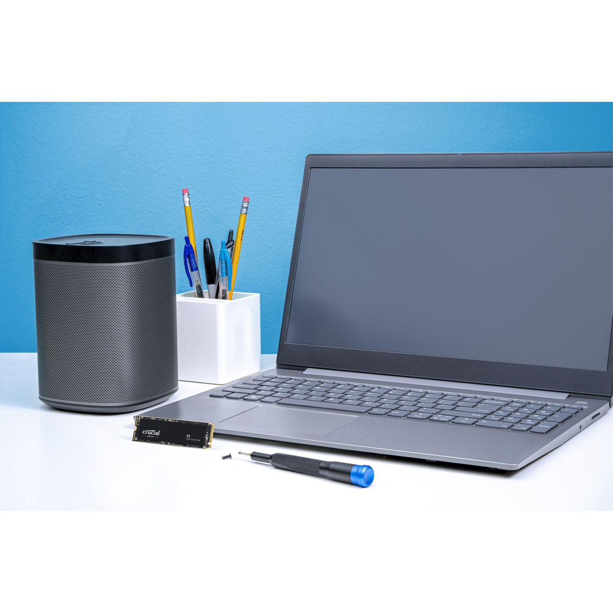 Laptop, luidspreker, potloden en schroevendraaier op een wit oppervlak met een blauwe achtergrond.