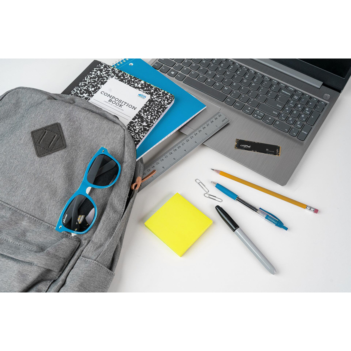 Plecak, laptop, notatniki, długopis, ołówek, okulary przeciwsłoneczne i inne przybory szkolne na białej powierzchni.