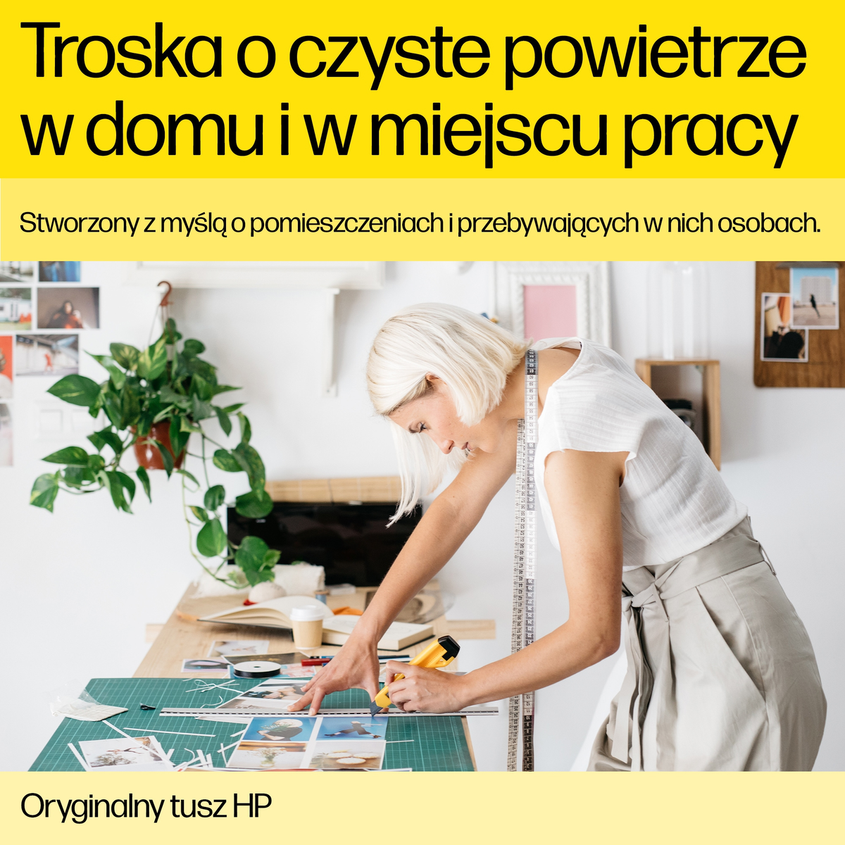 Kobieta wycina zdjęcia na stole. W tle roślina. Tekst u góry mówi: 'Czyste powietrze w domu i w pracy'.