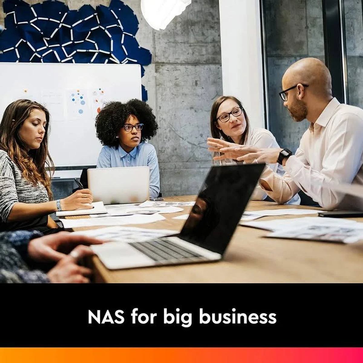 Quattro persone in riunione discutono di affari. Testo 'NAS for big business'.