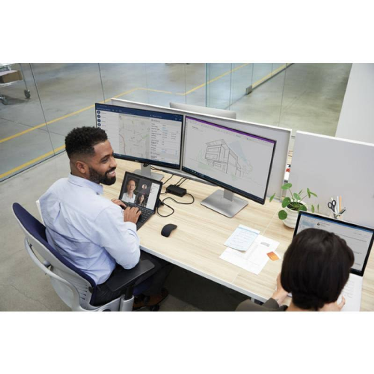 Dwie osoby w biurze korzystające z komputerów, z rozmową wideo na ekranie.