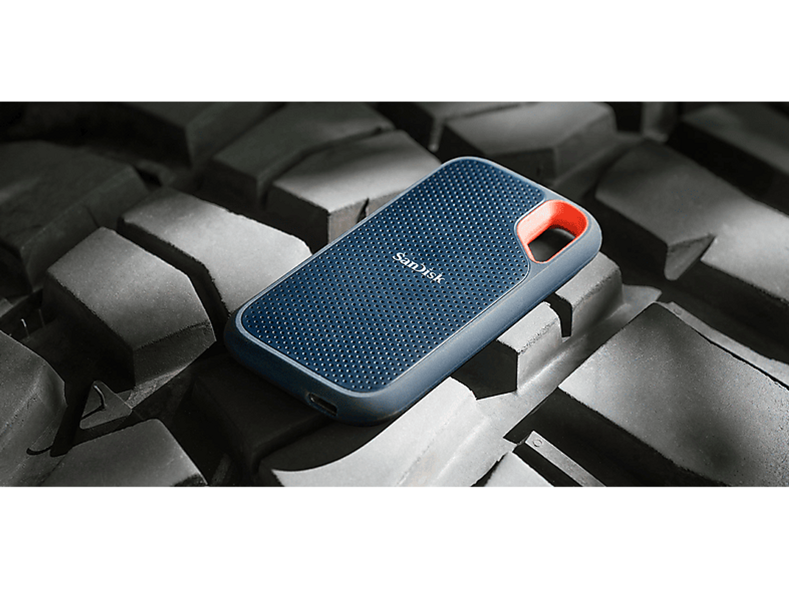 Ciemnoniebieski dysk zewnętrzny Sandisk na teksturowanej szarej powierzchni. Pomarańczowy akcent z boku.