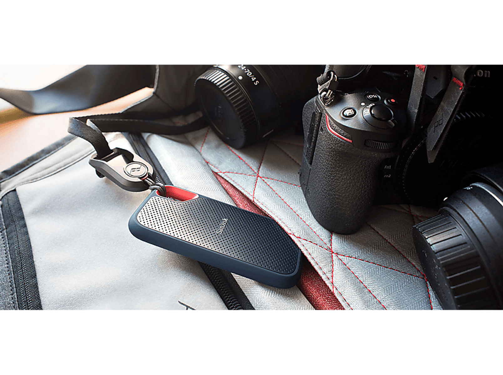 Czarny i czerwony zewnętrzny dysk twardy ze smyczą obok aparatów i akcesoriów na jasnoszarej powierzchni.