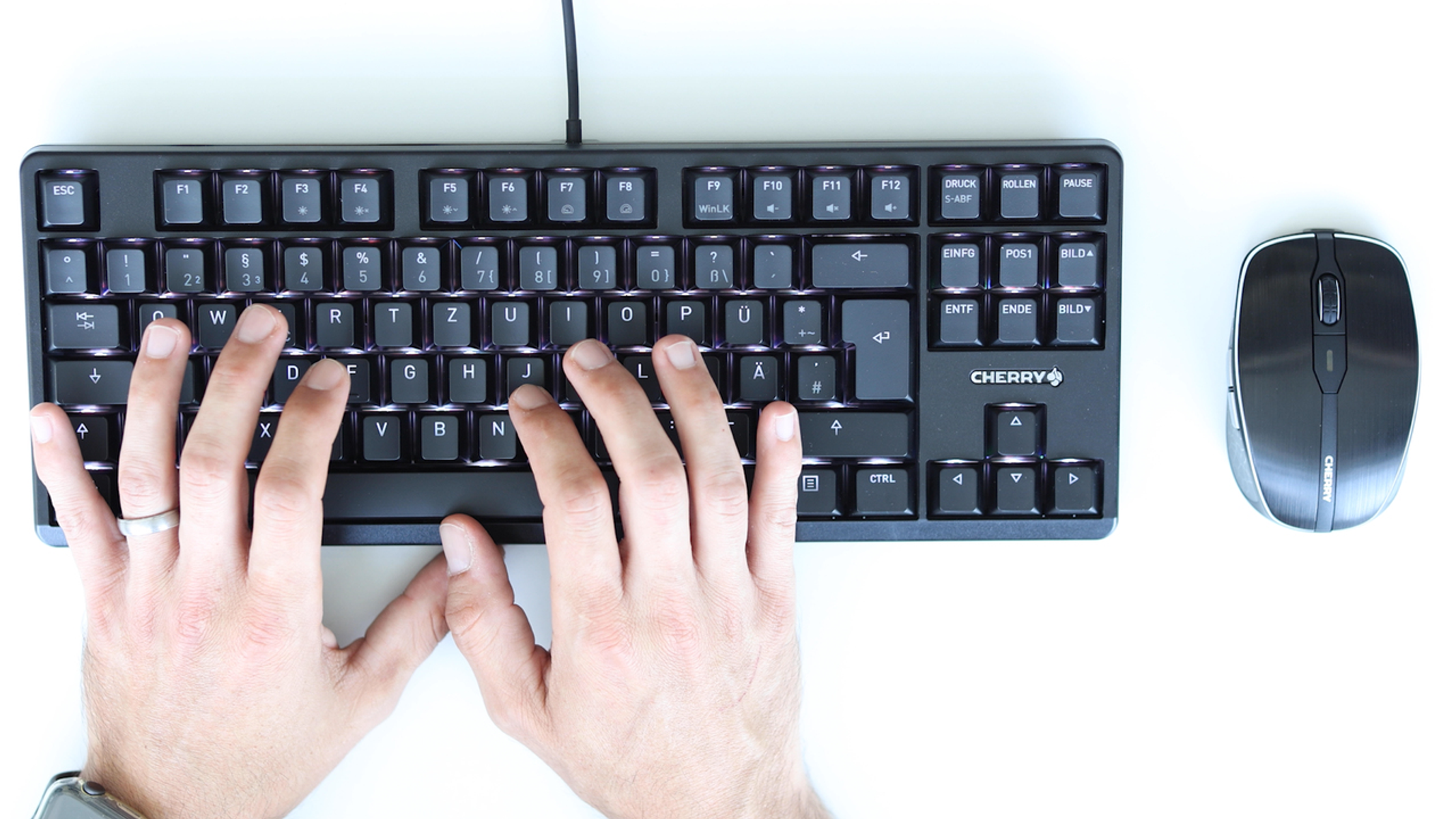 Ręce piszące na czarnej klawiaturze mechanicznej obok czarnej myszy.