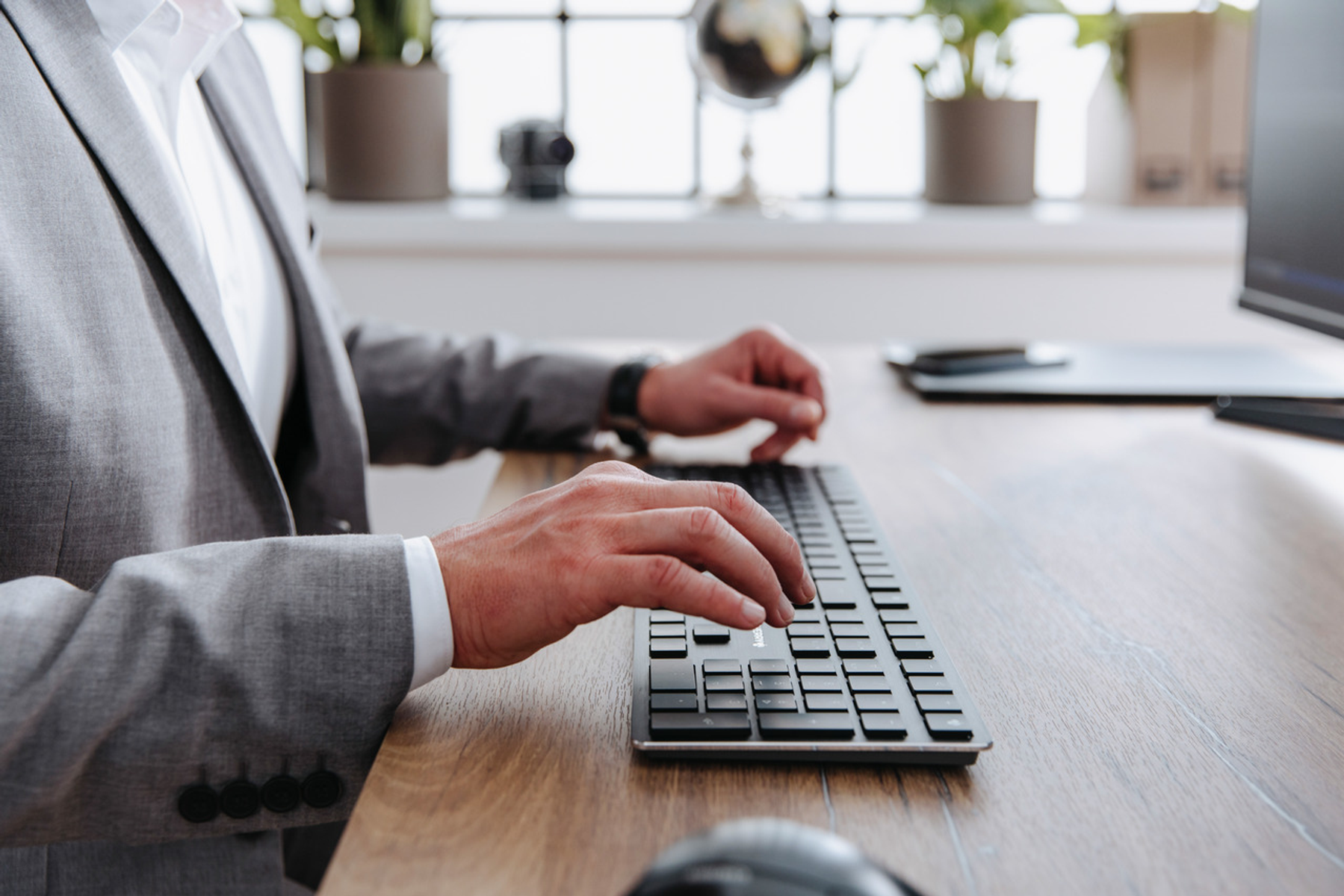 Dłonie osoby piszącej na czarnej klawiaturze na drewnianym biurku.