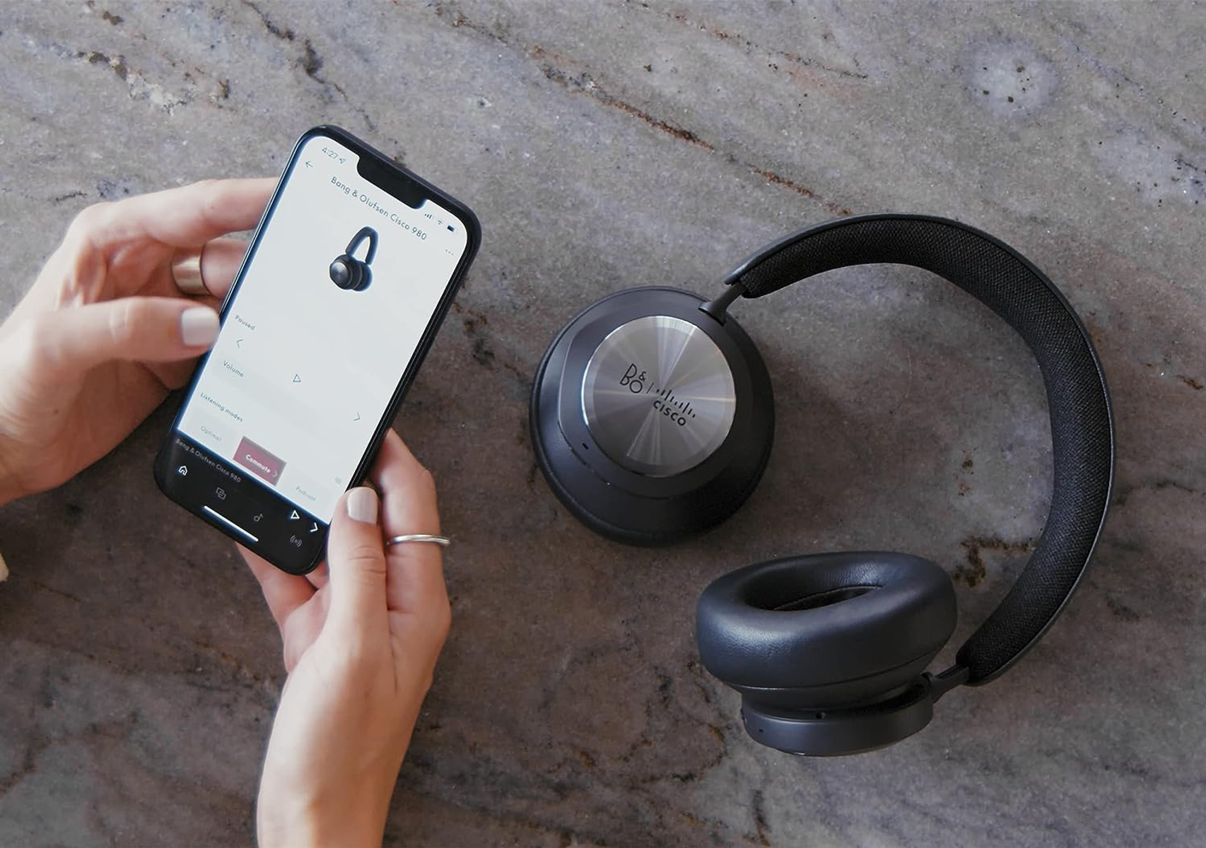 Die Hände einer Person, die ein Smartphone mit Kopfhörern hält. Ein Kopfhörerpaar liegt auf dem Tisch, Draufsicht.