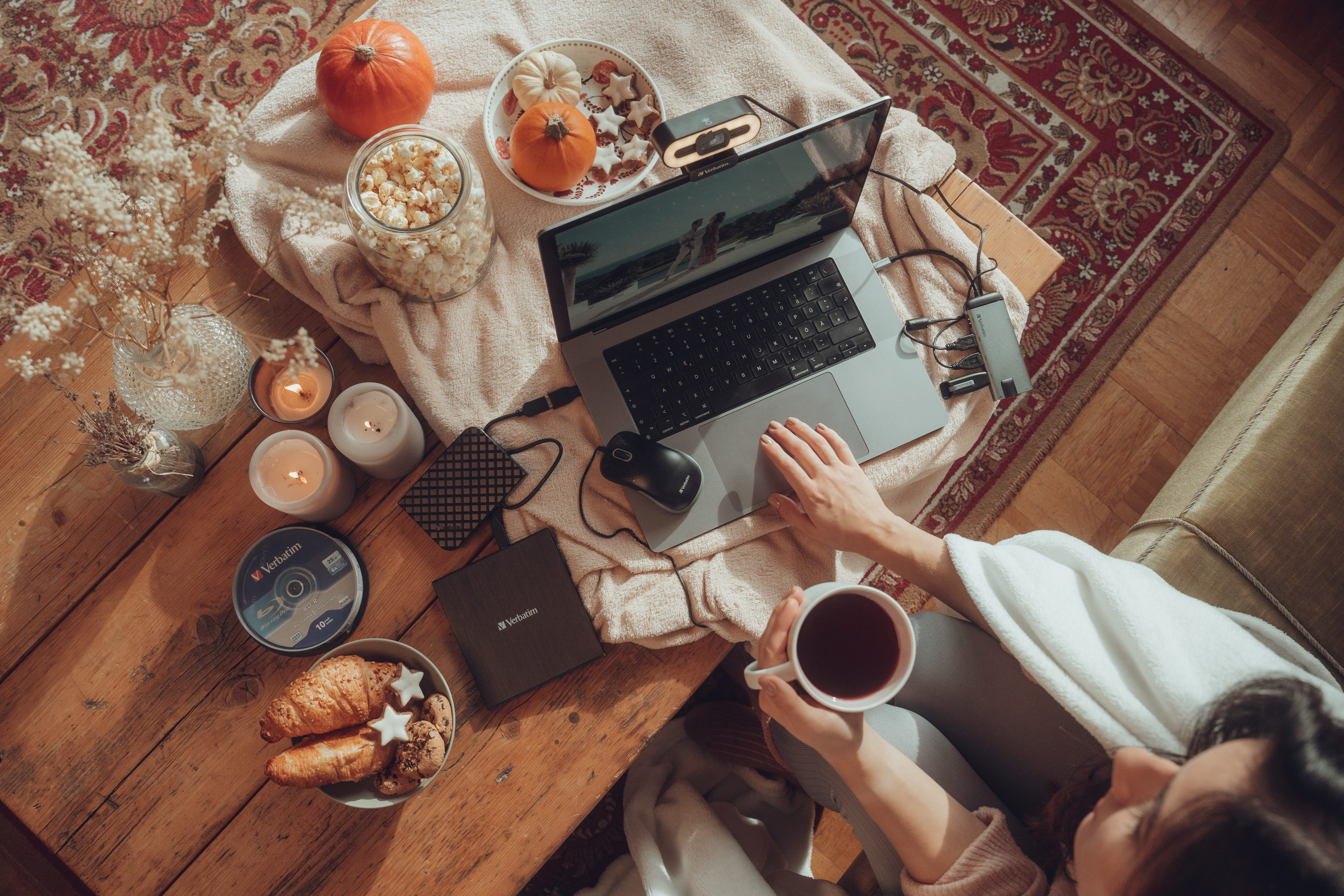 Osoba z filiżanką herbaty w pobliżu laptopa z jedzeniem i świecami na drewnianym stole.