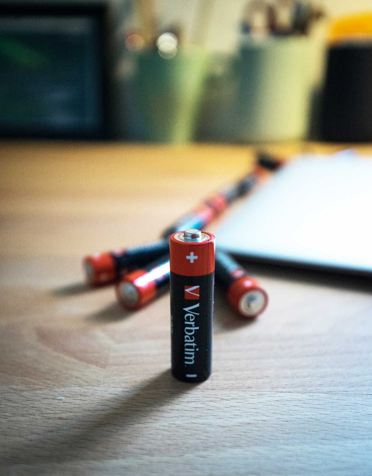 Zwarte en rode Verbatim AA-batterij staat op, andere liggen erachter. Houten tafel.