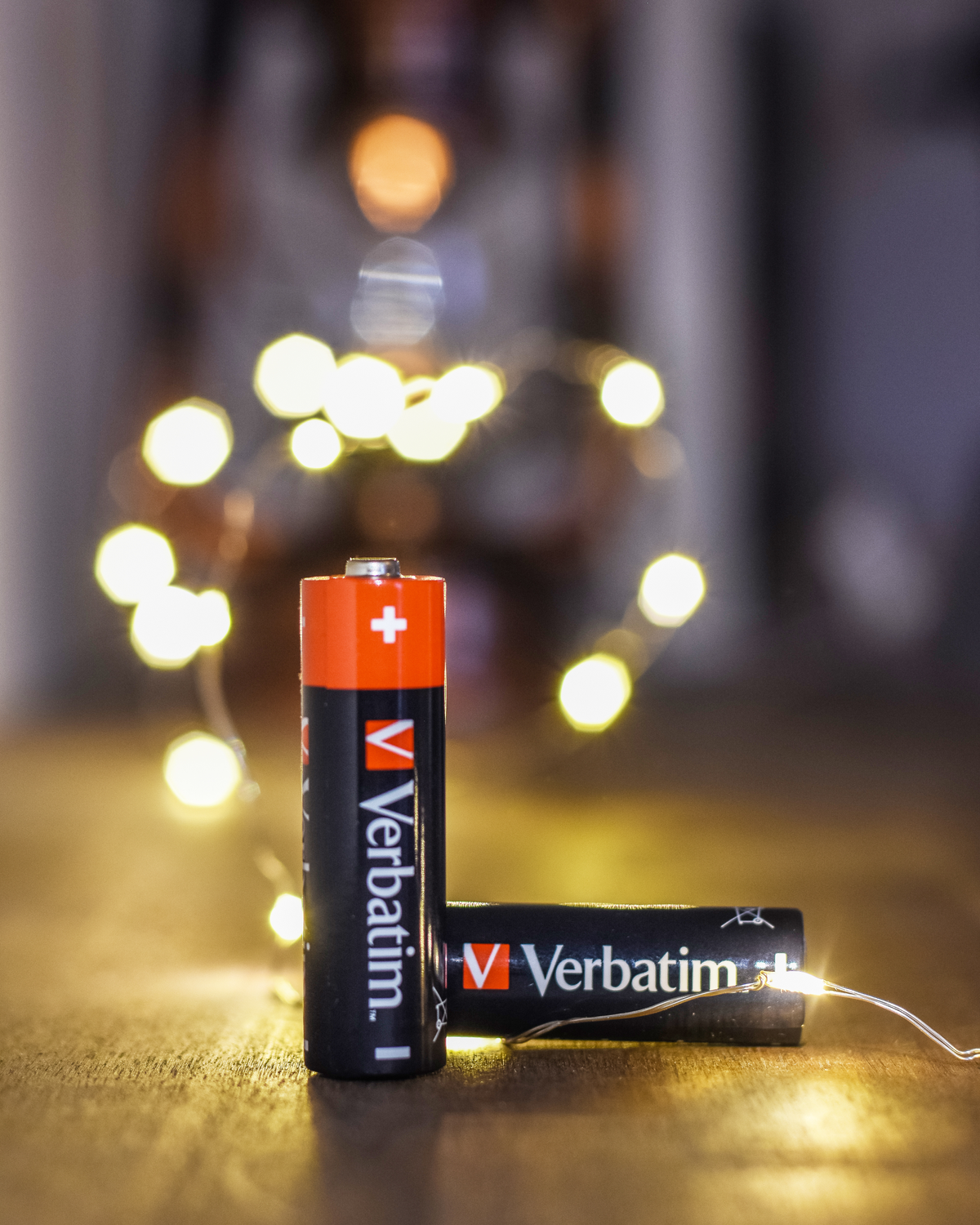 Deux piles Verbatim noires et oranges près de guirlandes lumineuses sur une surface en bois.