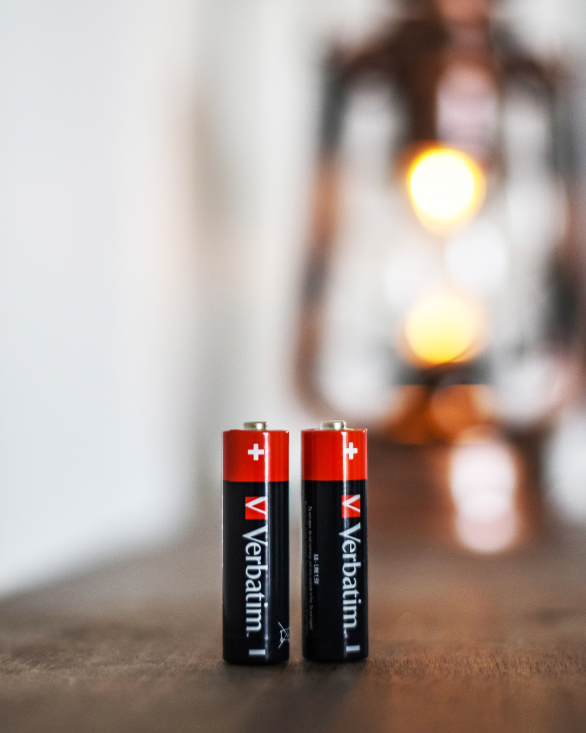 Twee Verbatim AA-batterijen staan op een houten oppervlak. Ze zijn zwart met rode en witte details.