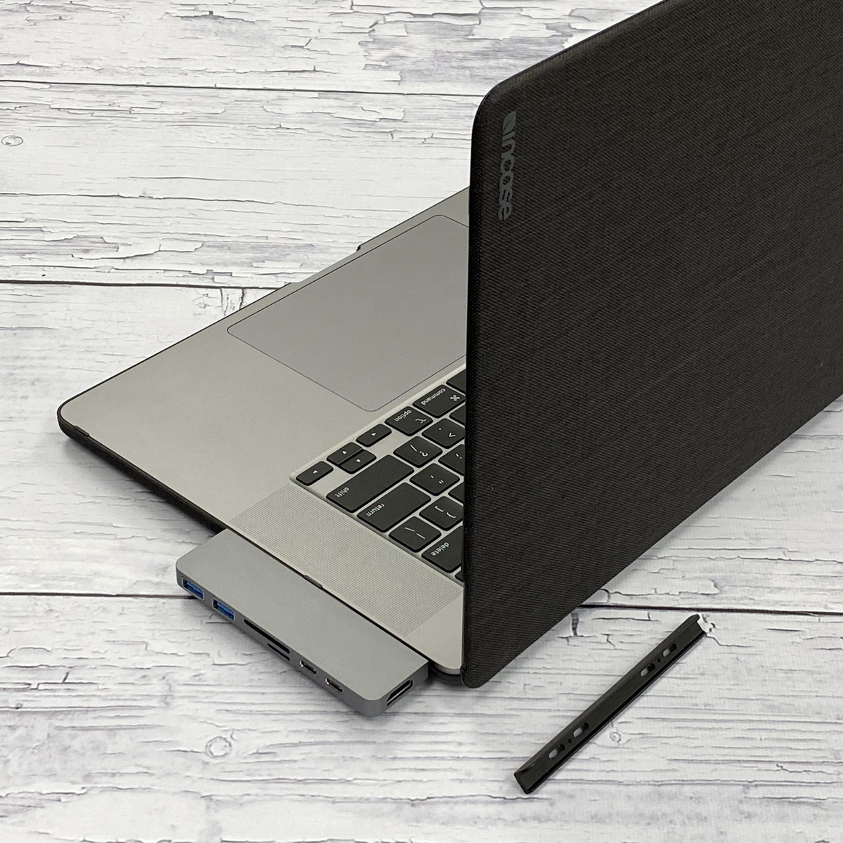 Ein Laptop mit Hülle, Hub und schwarzem Stift auf Holzoberfläche.