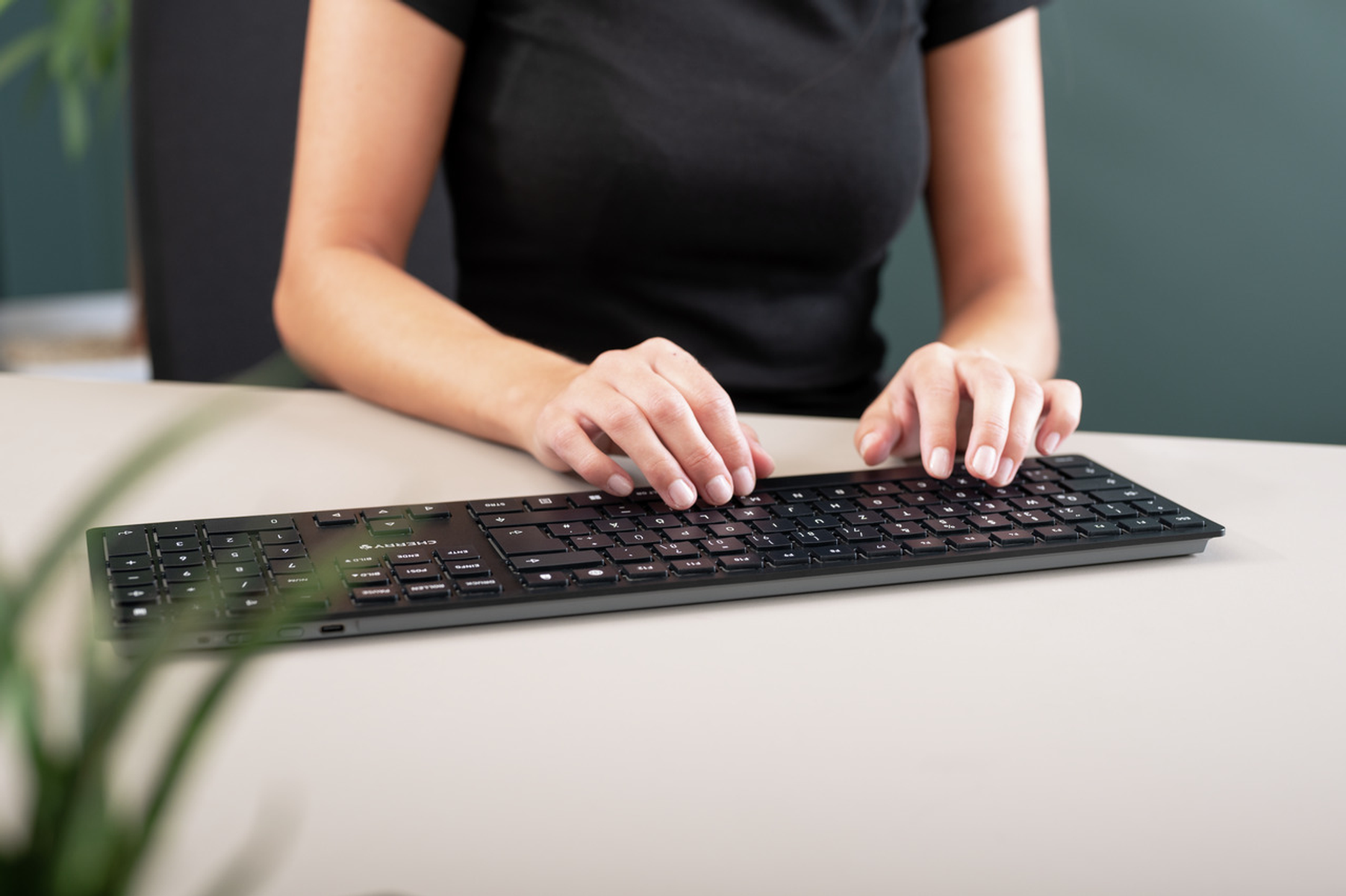 Kobieta pisze na czarnej klawiaturze. Ręce na klawiaturze, przed zieloną ścianą.