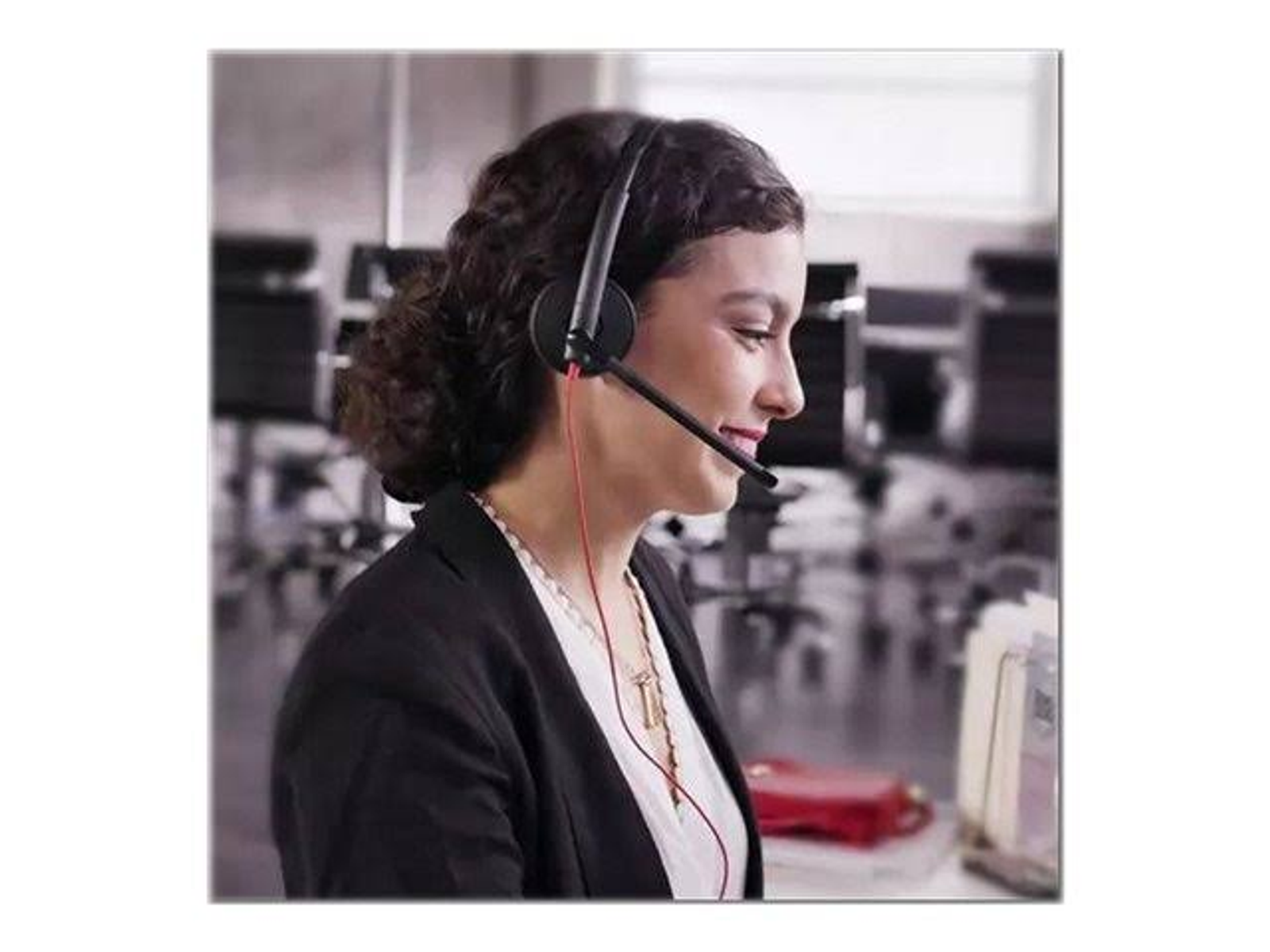 Kobieta w słuchawkach uśmiecha się i pracuje przy biurku. W tle jest szafa na dokumenty.