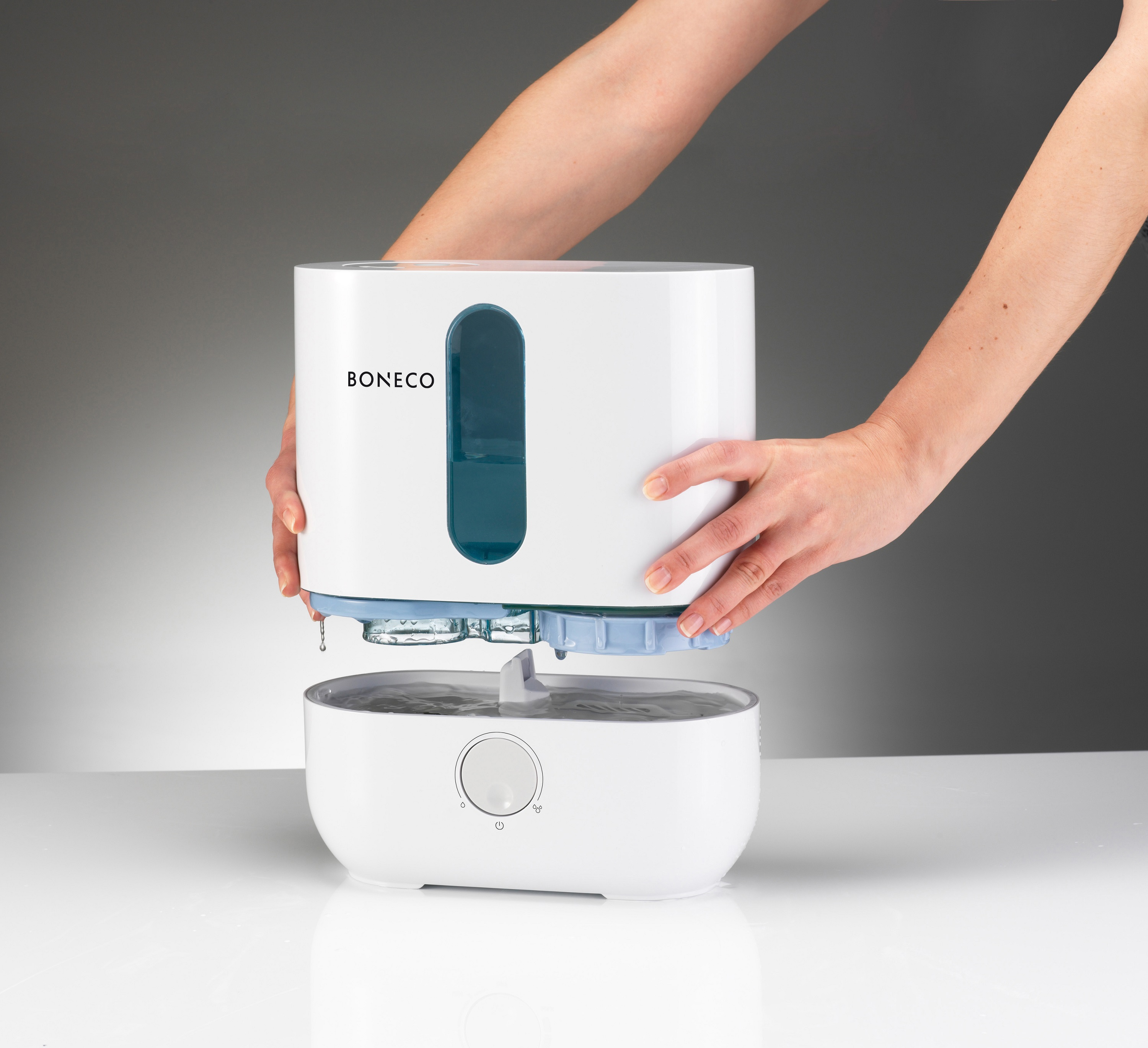 Manos ensamblando un humidificador blanco. La parte superior se está colocando sobre la unidad base.