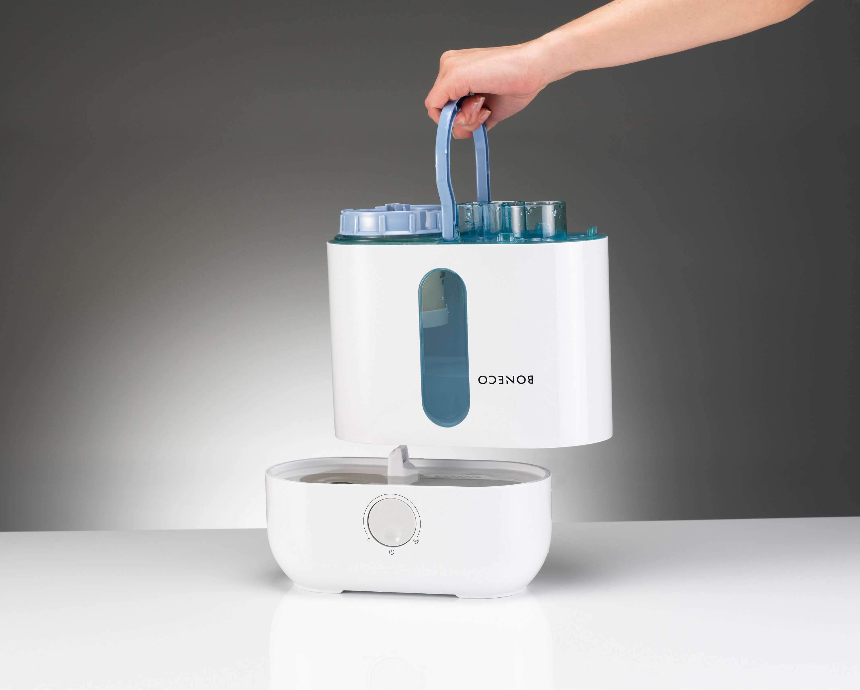 Una mano levanta la sección superior de un humidificador blanco y azul, separándola de la base.