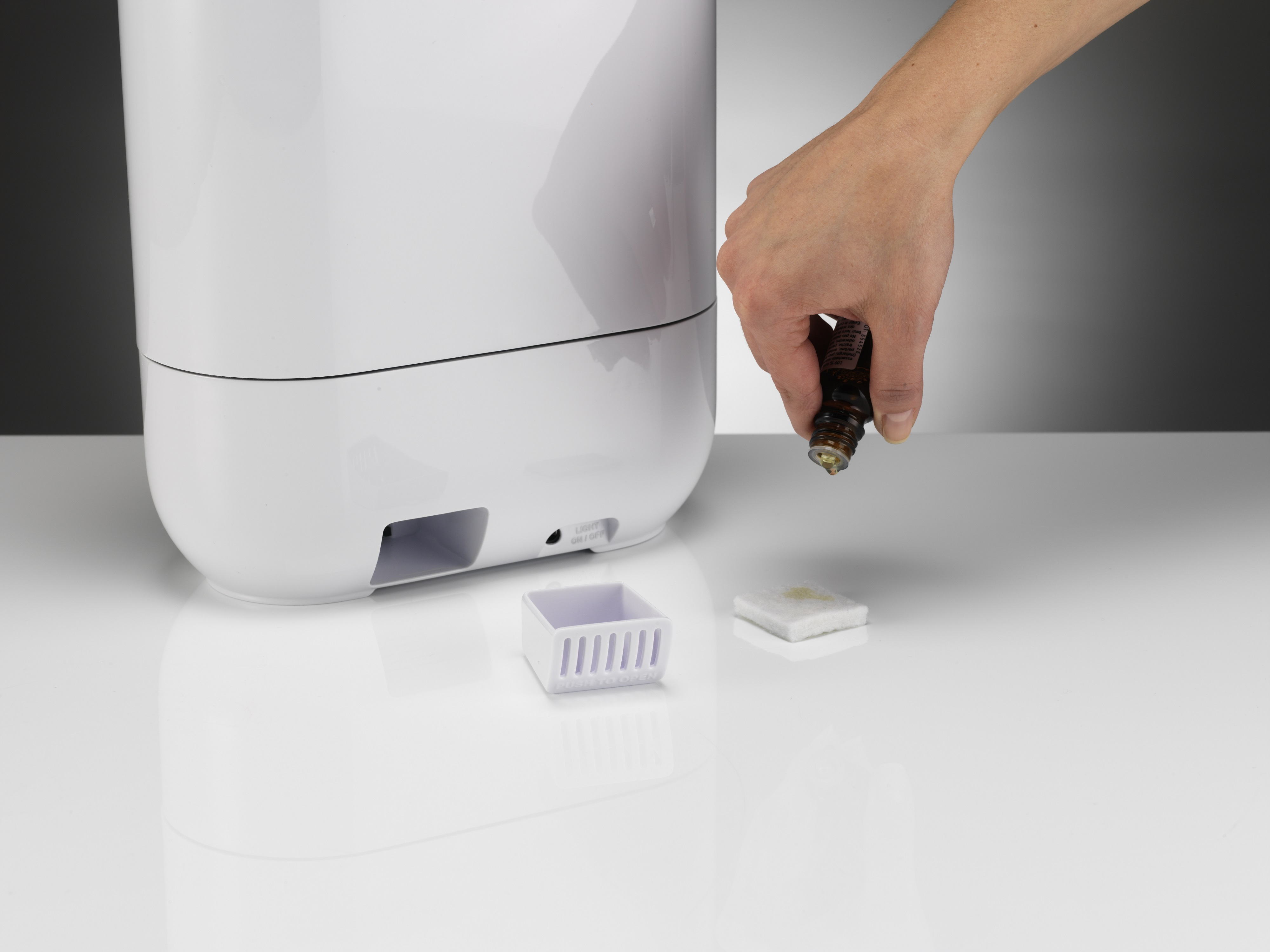 Una mano añade aceite esencial a un humidificador blanco. Fondo blanco.